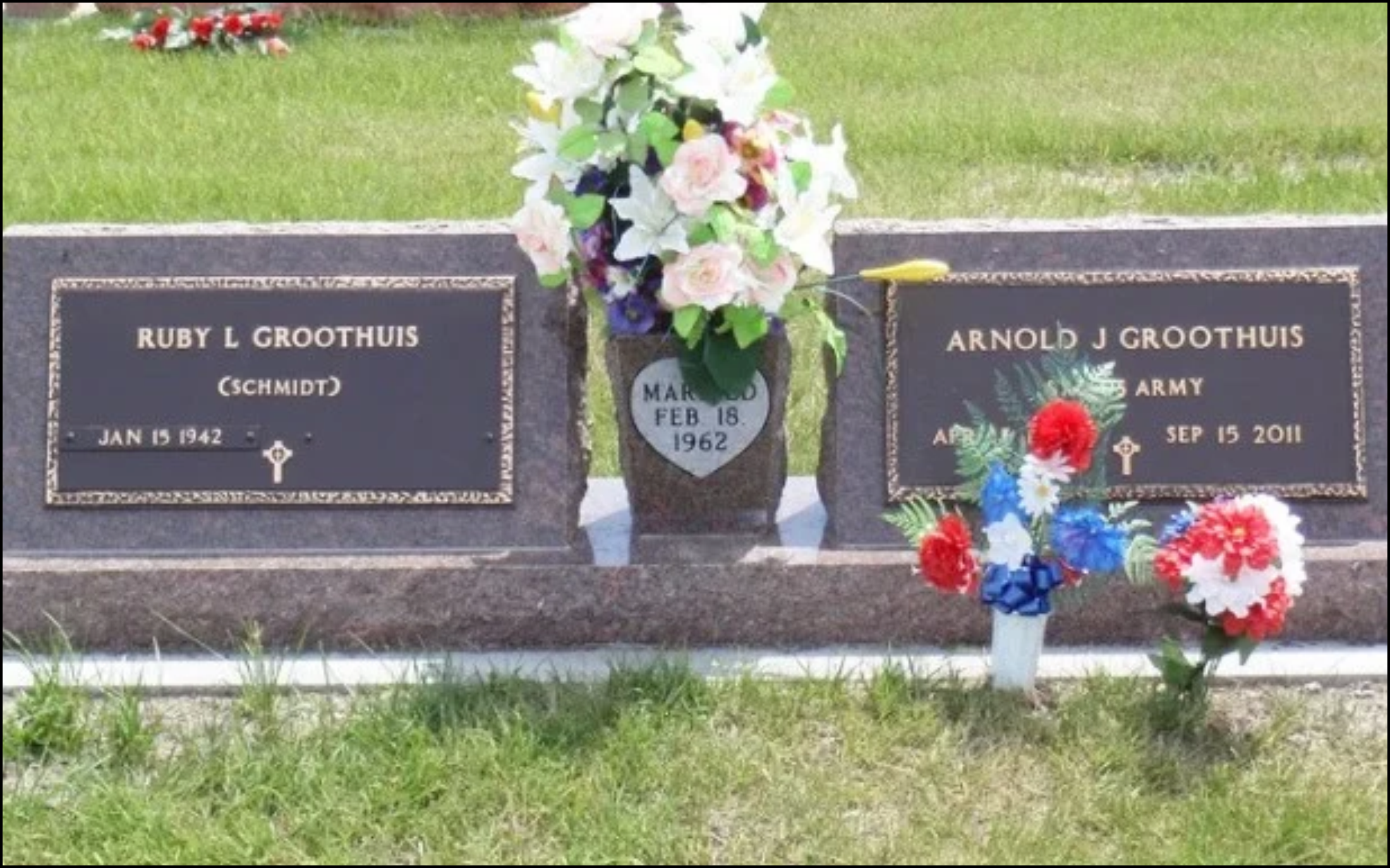 Gravestone for Ruby L. Groothuis and Arnold J. Groothuis, decorated with flowers and wreaths, in a cemetery with grass in the background.