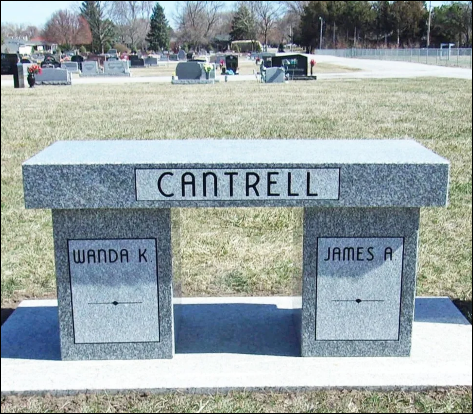 A granite memorial bench at a cemetery with the name 'CANTRELL' engraved on it. The bench has two side panels with the names 'WANDA K.' and 'JAMES A.' engraved on them.