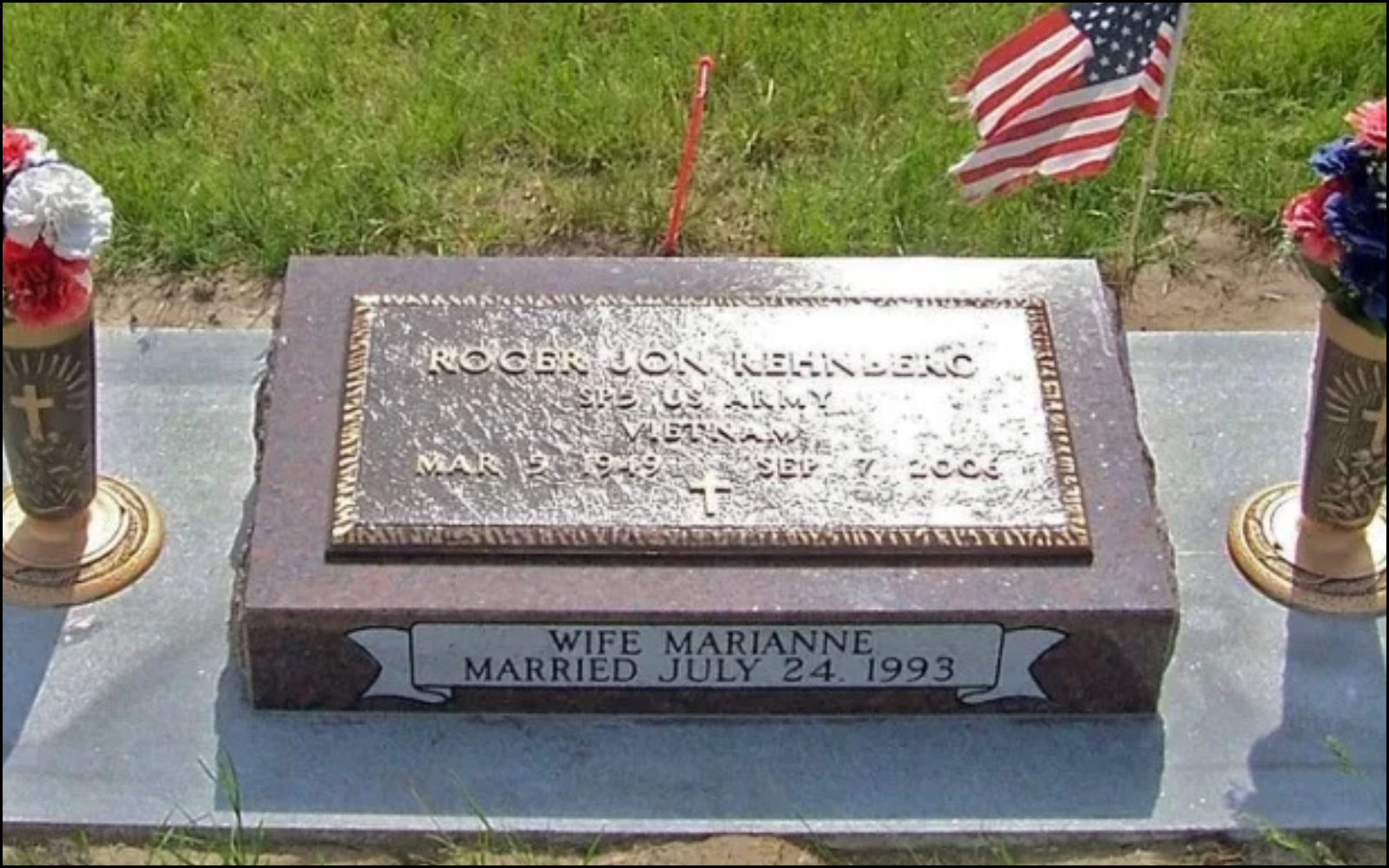 A gravesite memorial for Roger Jon Rhenberg, who served in the U.S. Army. The headstone displays his name, service information, and the dates March 2, 1949, to September 7, 2002. It also mentions his wife, Marianne, married on July 24, 1993. The grave is decorated with American flags and flower vases.
