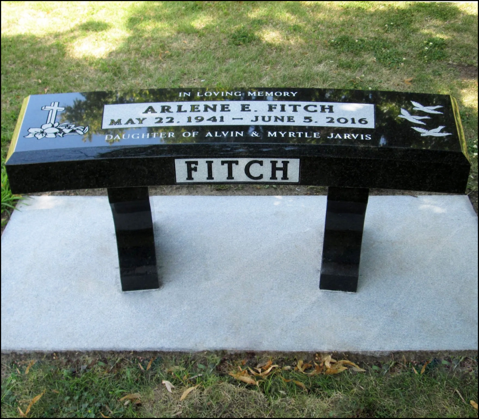 A black and white polished granite grave marker with a white background, honoring Arlene E. Fitch, who lived from May 22, 1941 to June 5, 2016. It features a cross with flowers and three birds in flight.