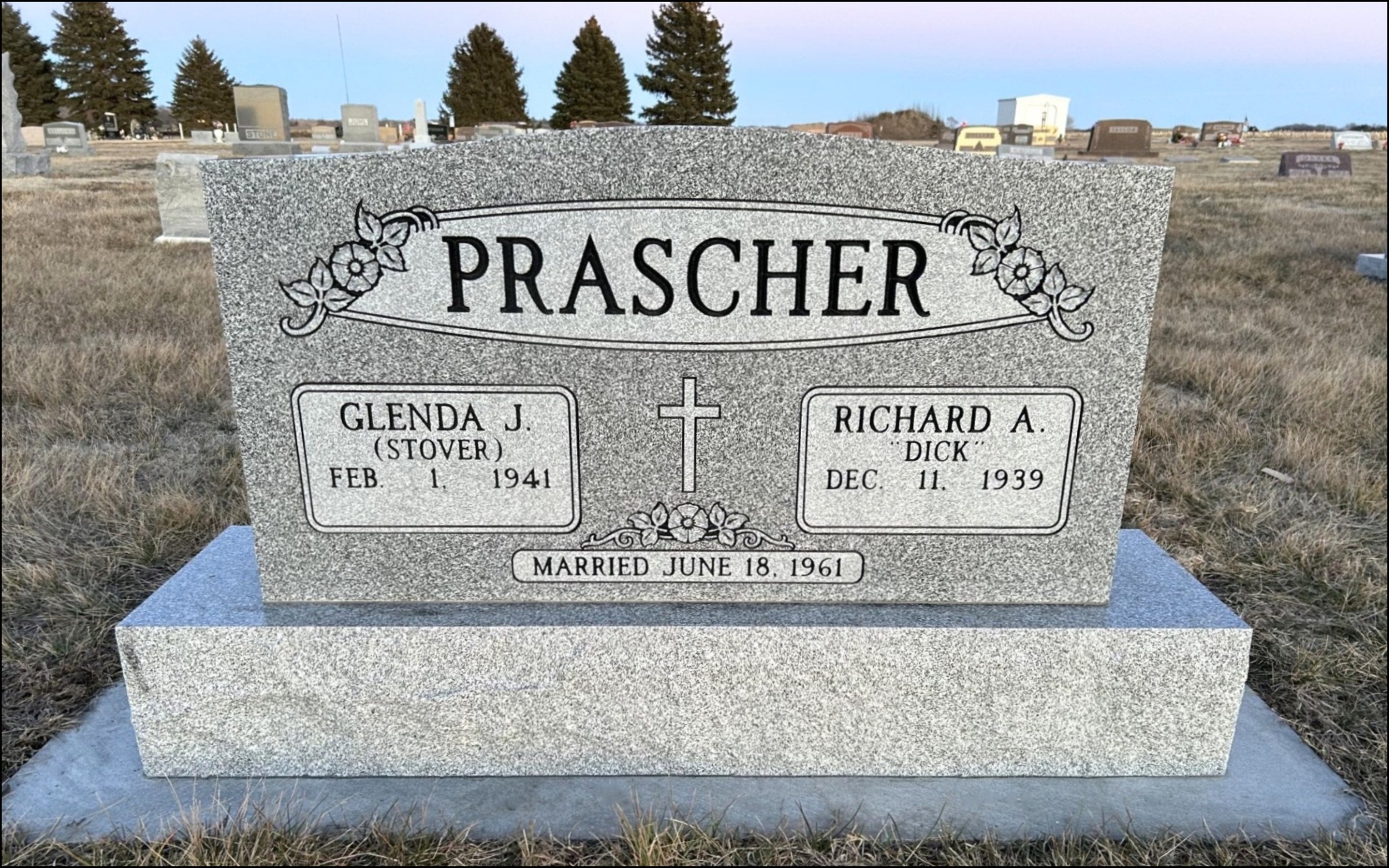 Gravestone for Glenda J. Prascher (Stover), born February 1, 1941, and Richard A. Dick, born December 11, 1939, in a cemetery with other headstones and trees in the background.