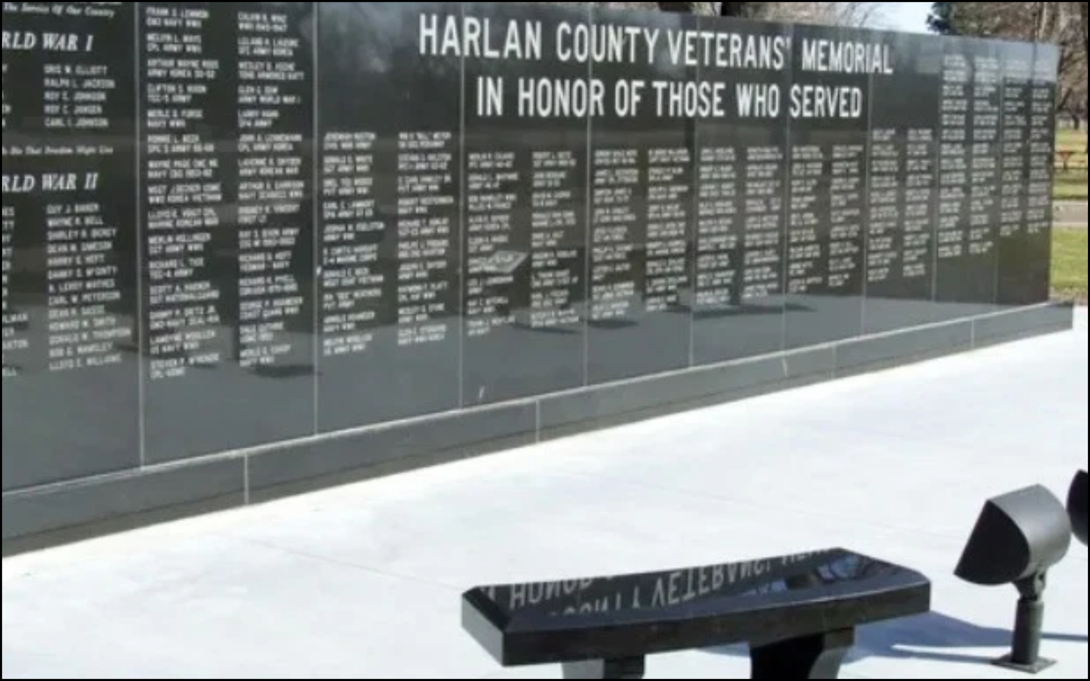 A memorial wall with names of veterans, titled 'Harlan County Veterans Memorial,' honoring those who served in World War I and World War II, outdoors with trees in the background.