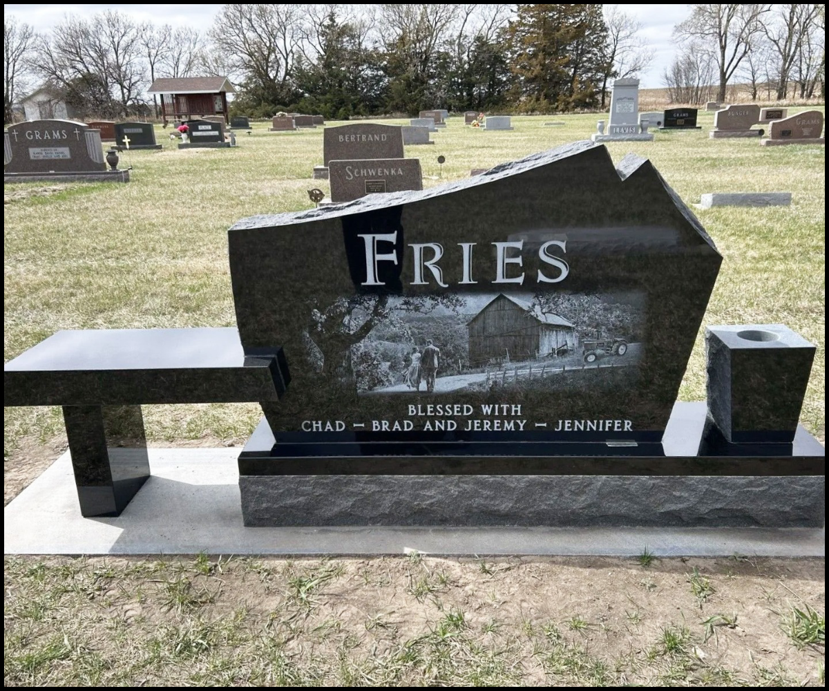 A headstone in a cemetery with the name 'Fries' and an image of a barn, two people, and a car. It is inscribed with blessings for Chad, Brad, Jeremy, and Jennifer.