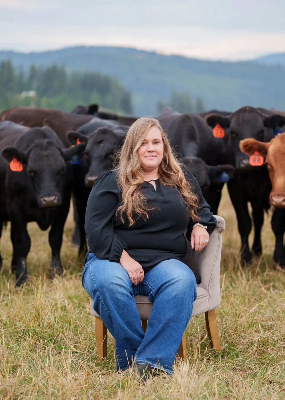 Woman seated in a field with a herd of cattle and mountains in the background