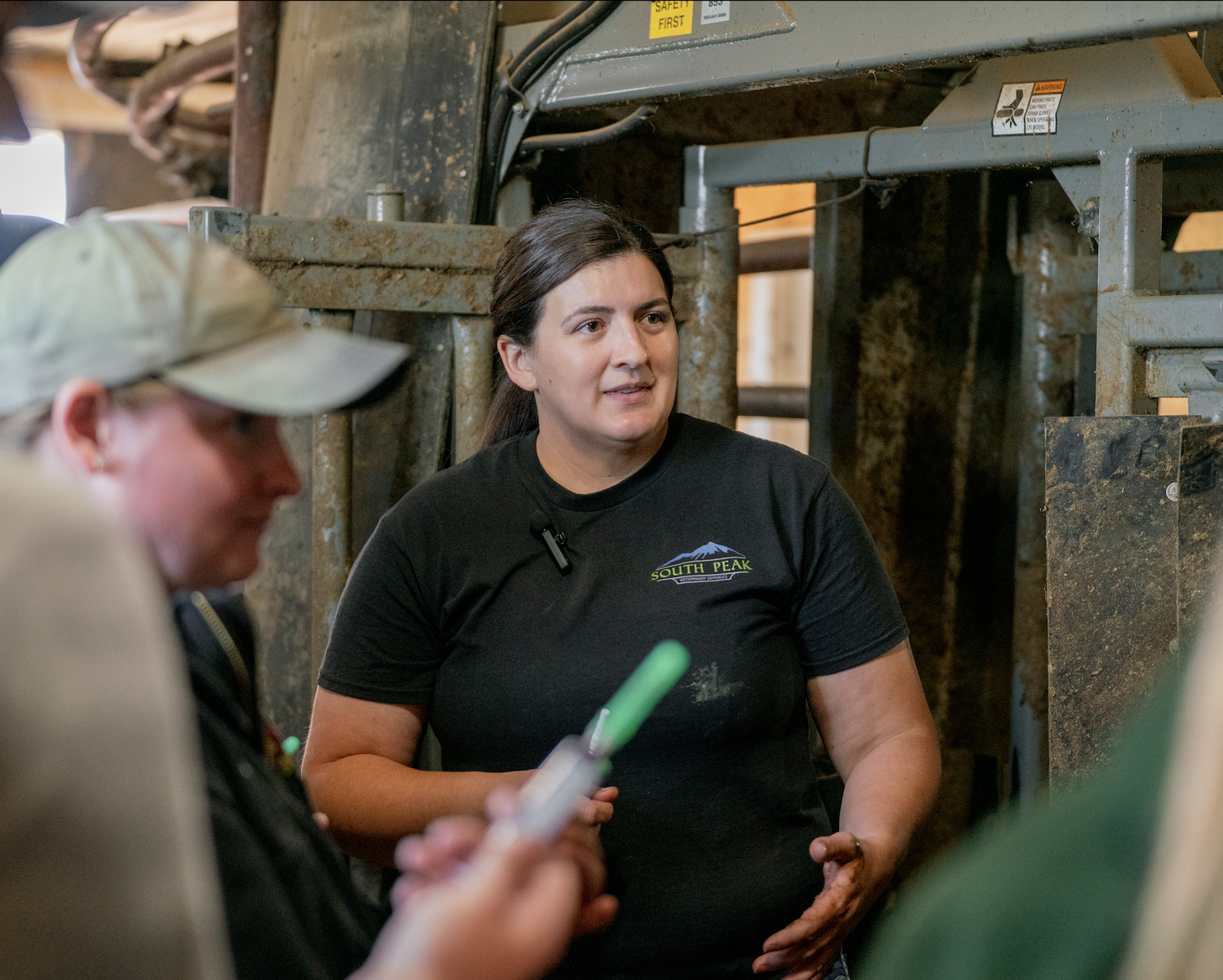 Woman in a South Peak Veterinary Services shirt speaking inside an industrial livestock facility