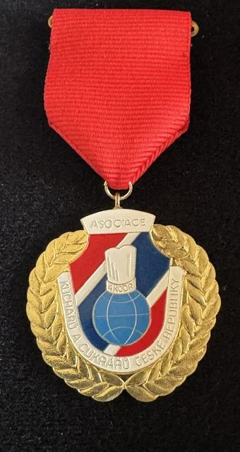 Medal with a red ribbon and a gold laurel wreath border, featuring a blue and white target symbol and the words 'KULIGARA A UKRAH CUCHADANU CESHE REPUBLIKY'.