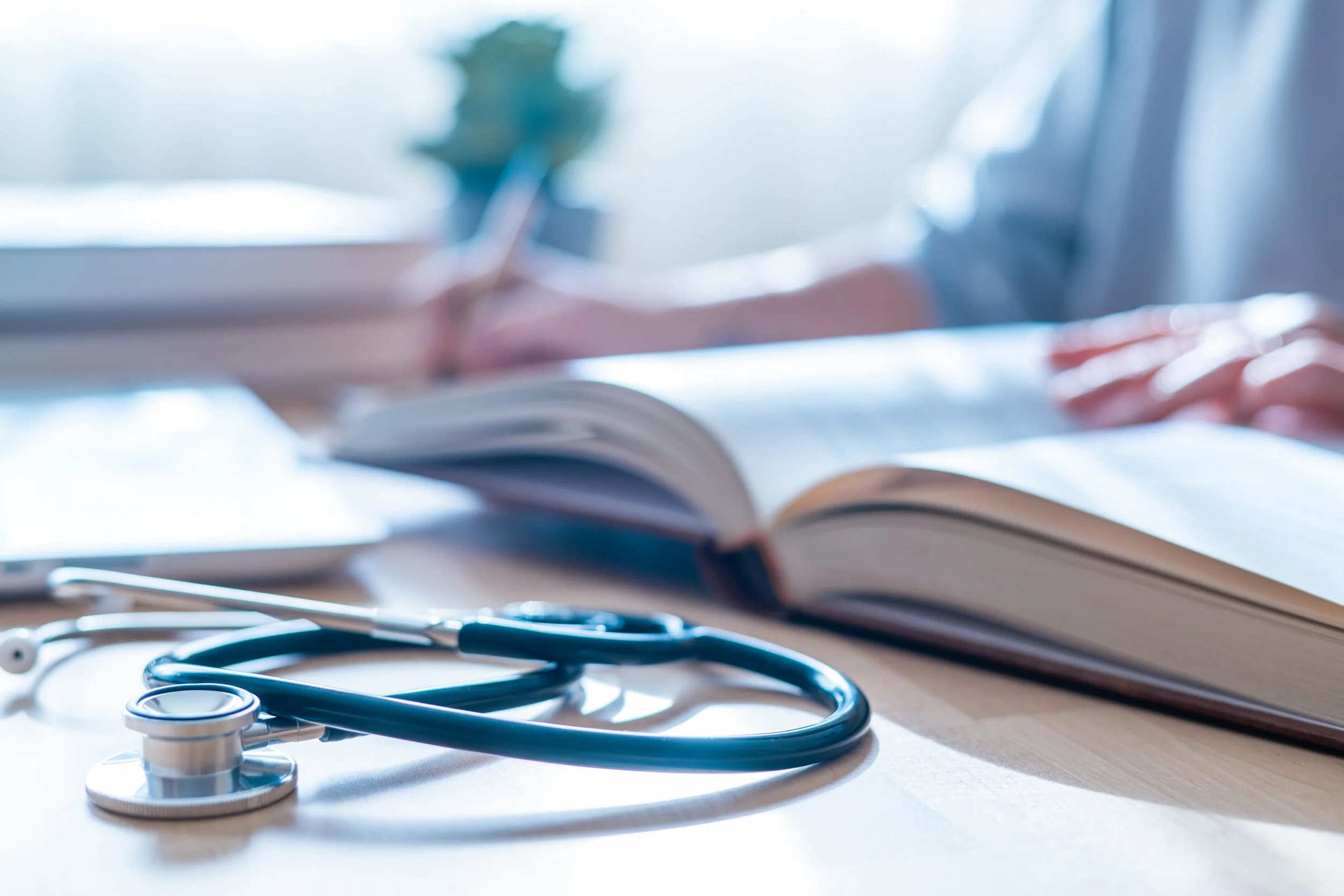 Medical stethoscope on a table with open books and a person's hand in the background.