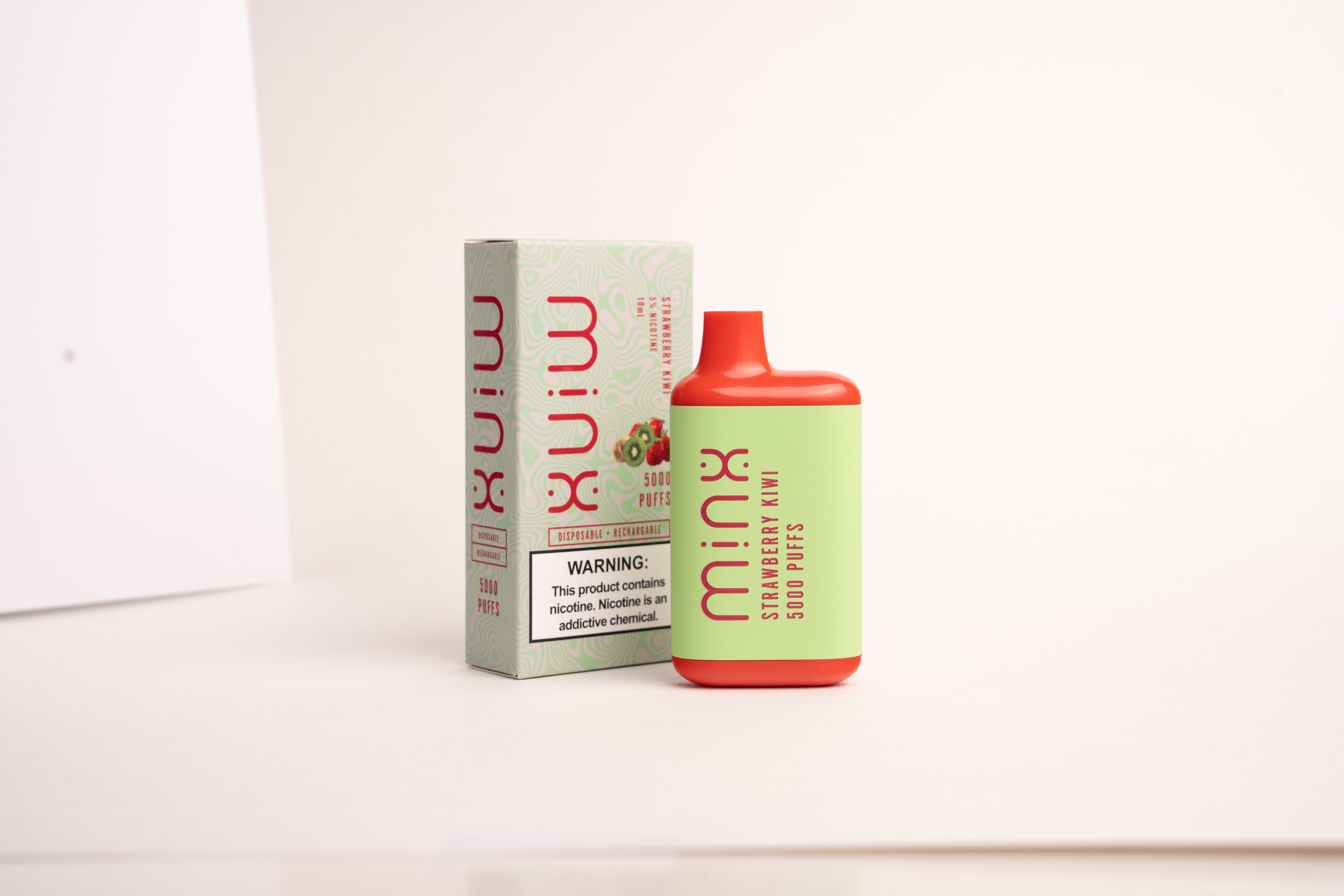 A Kohaku disposable vape bottle with a red cap and green label, positioned in front of its box, which displays a kiwi and strawberry flavor with 5000 puffs on a plain white background.