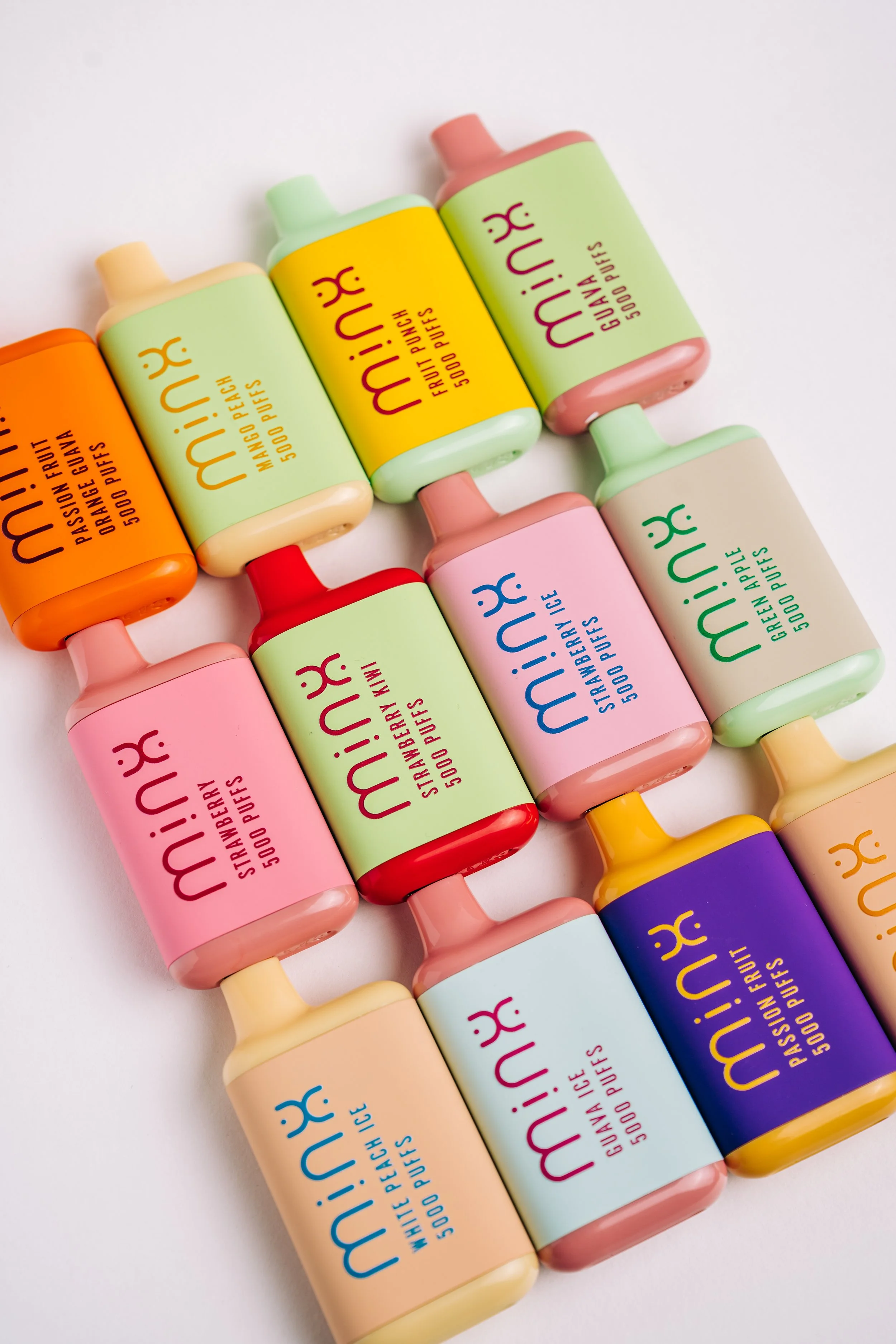 Colorful lip balm tubes with various flavors, including passion fruit, mango peach, fruit punch, green apple, strawberry, strawberry watermelon, white peach, guava, and passion fruit, arranged on a white surface.