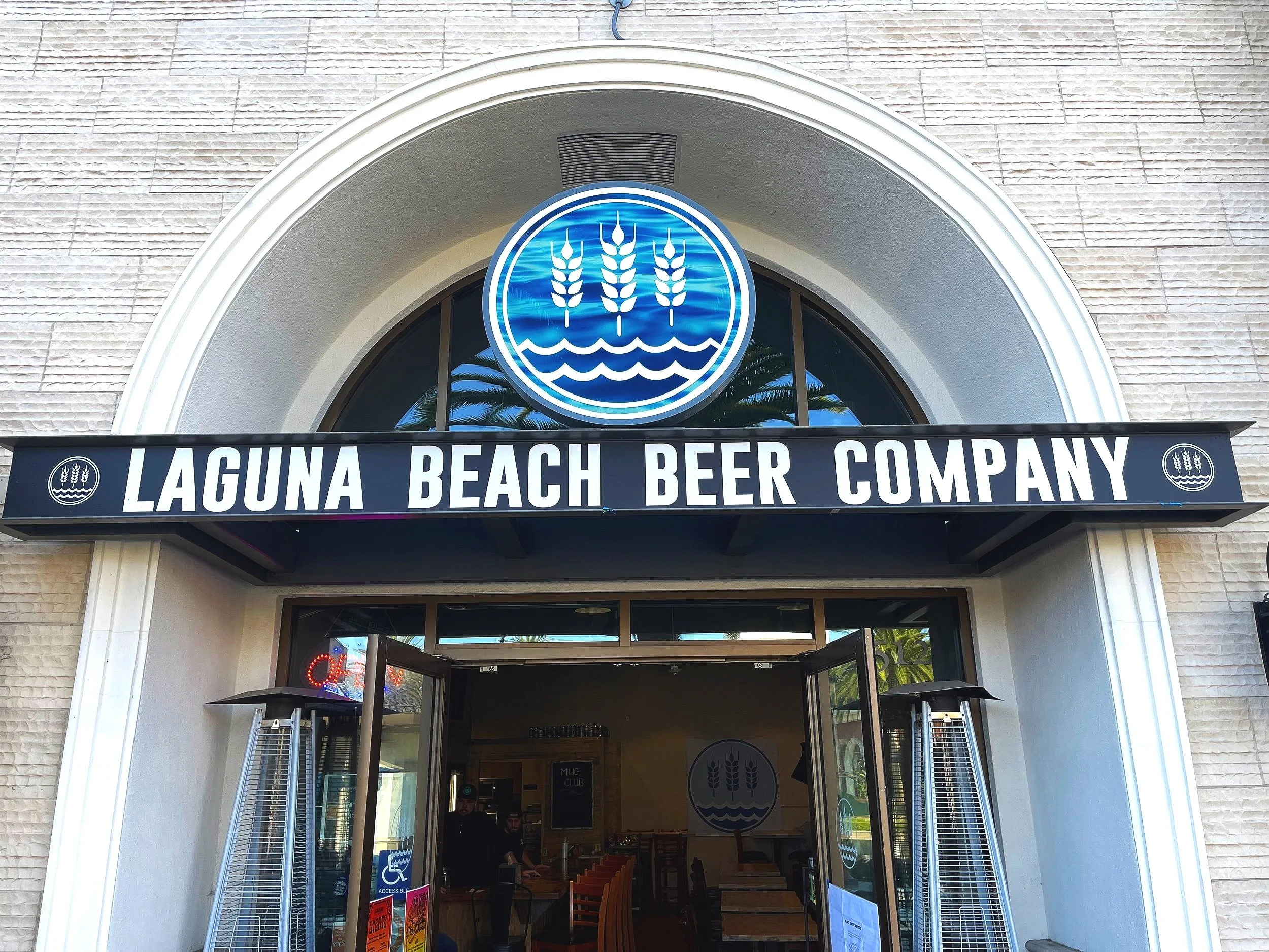 Exterior of the Laguna Beach Beer Company building with a sign, logo, and open doors showing the inside.