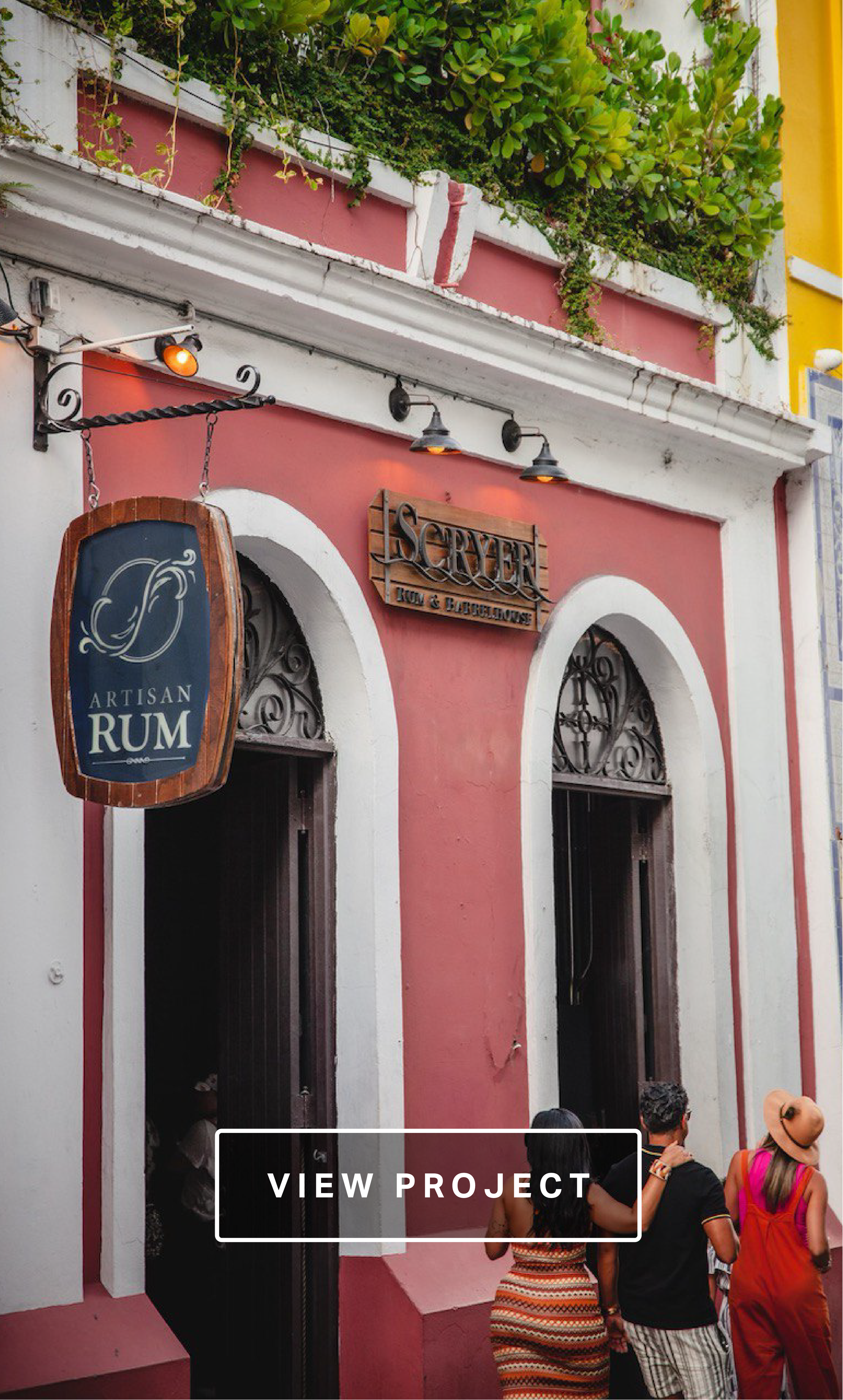 Facade of a bar with a pink and white exterior, signage for 'Server Rum & Bathehouse', and people standing outside including a woman in a striped dress and a man in a black shirt.