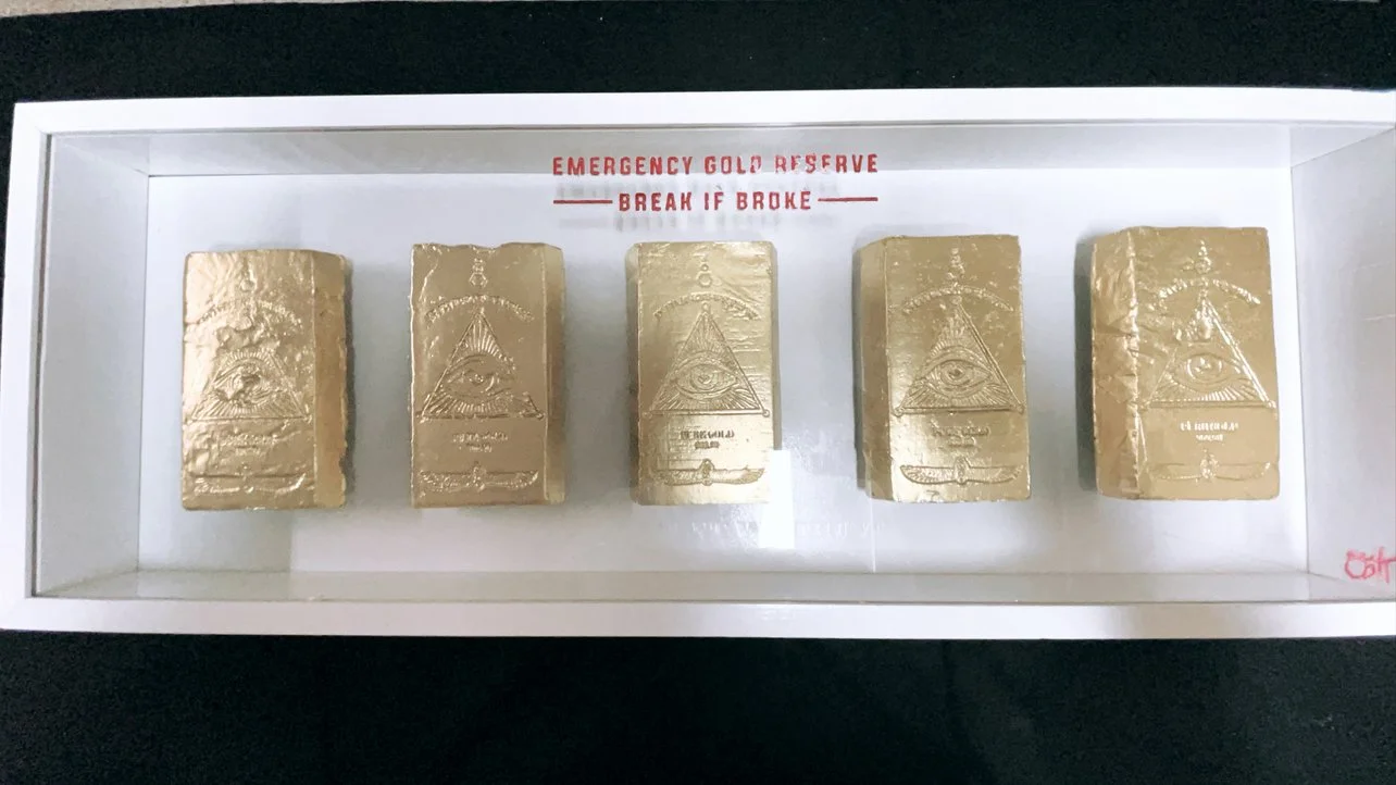 Five gold bars inside a display case labeled 'Emergency Gold Reserve' with a warning to break if broken.