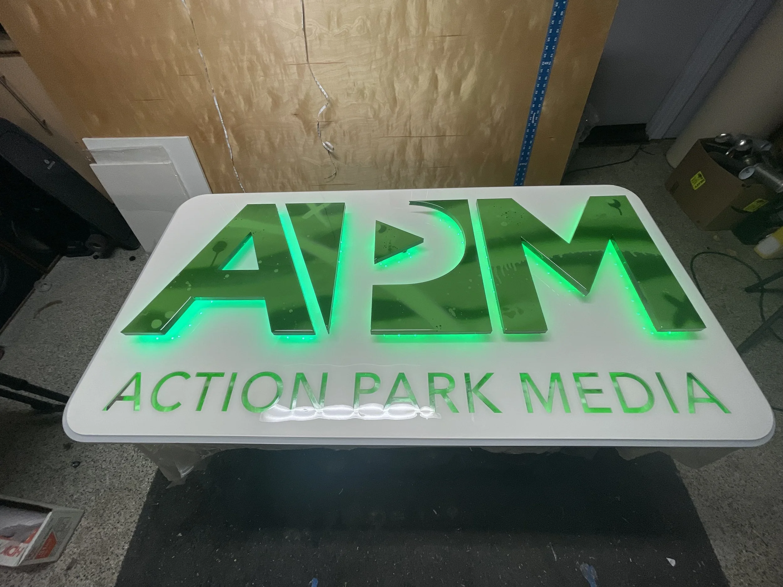 Illuminated sign with green letters reading 'APM' and 'ACTION PARK MEDIA' underneath.
