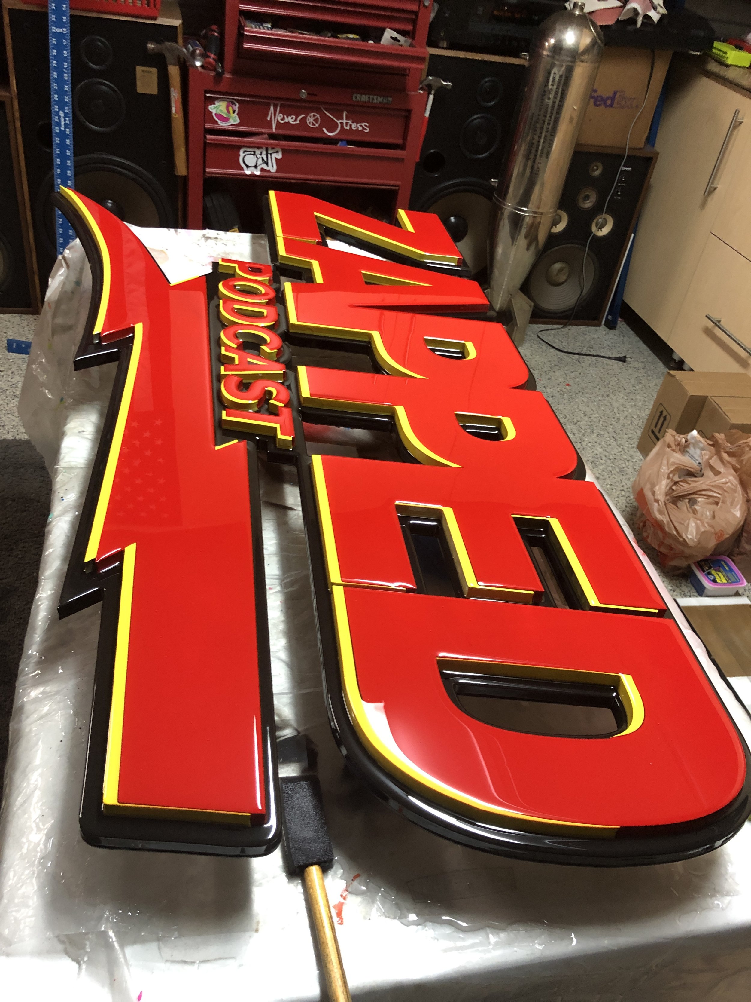 A red and yellow Chevrolet Poop Shop sign under construction on a plastic-covered work surface in a workshop, with tools and storage in the background.