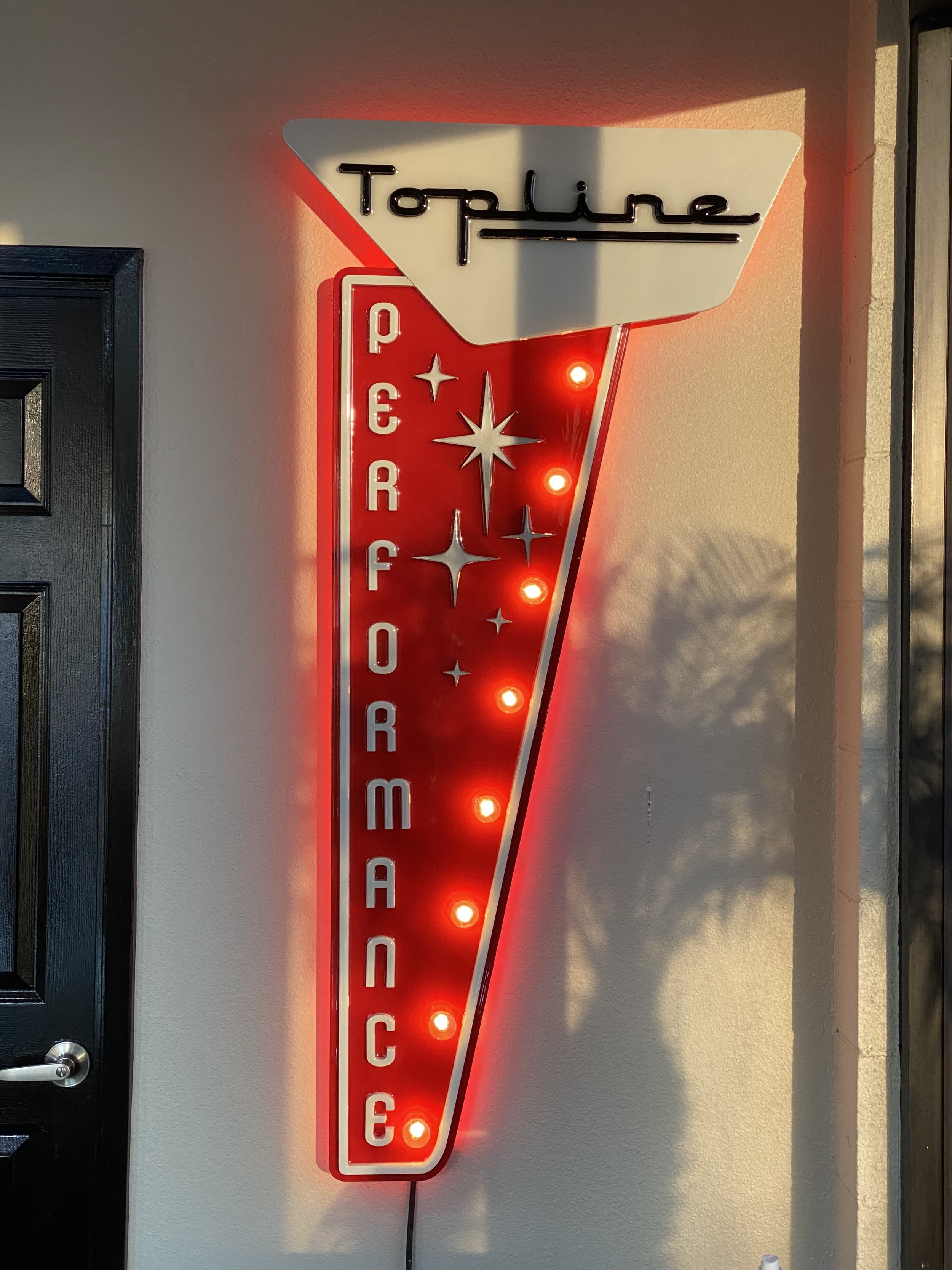 A vertically oriented neon sign reads 'Topline' at the top, with 'Performance' written vertically below. The sign features star designs and red lights, mounted on a wall.