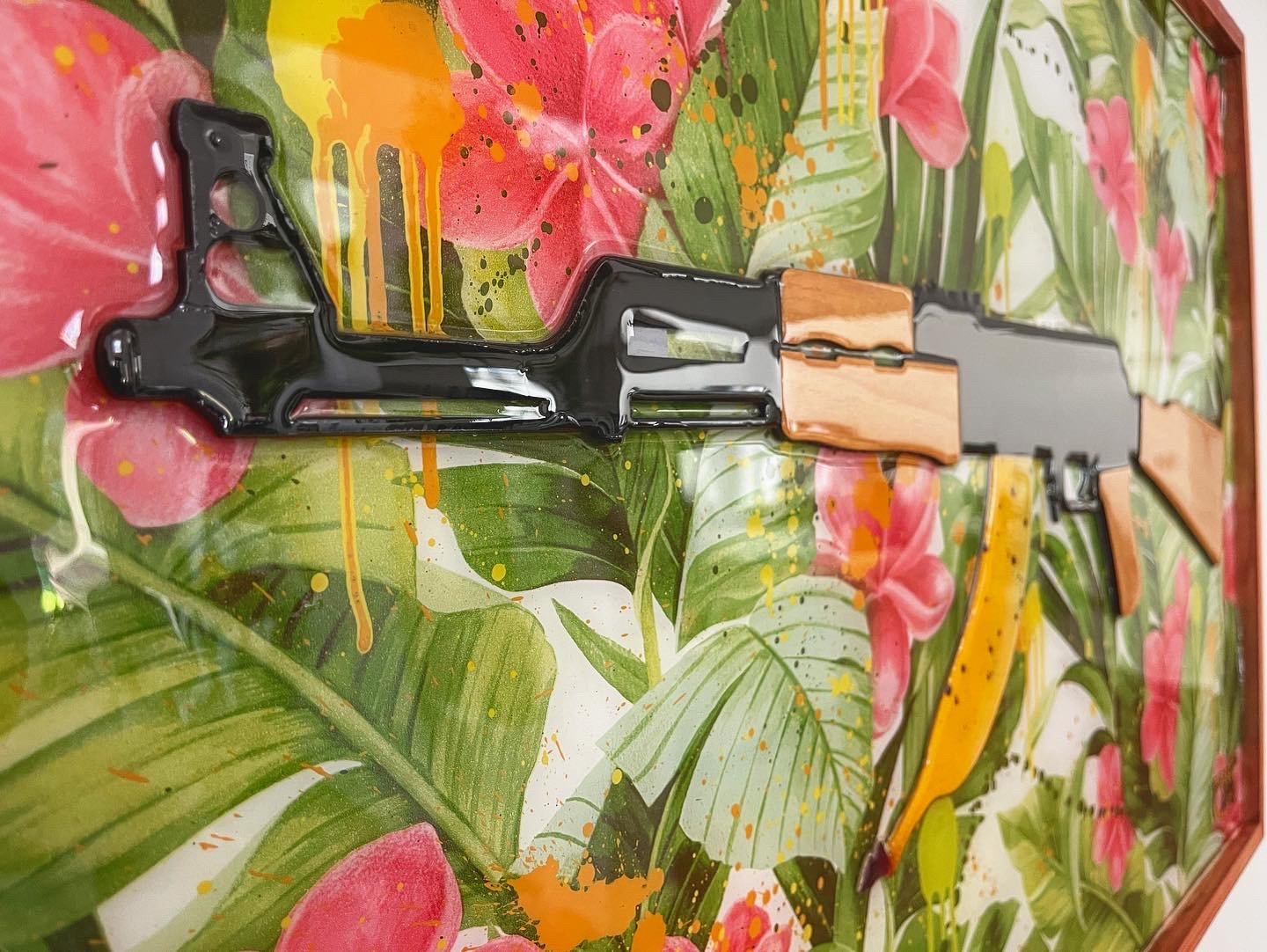 A colorful painting with large pink flowers, green leaves, and yellow accents. A black and wooden object, possibly a toy gun or a decorative piece, rests on the painting.