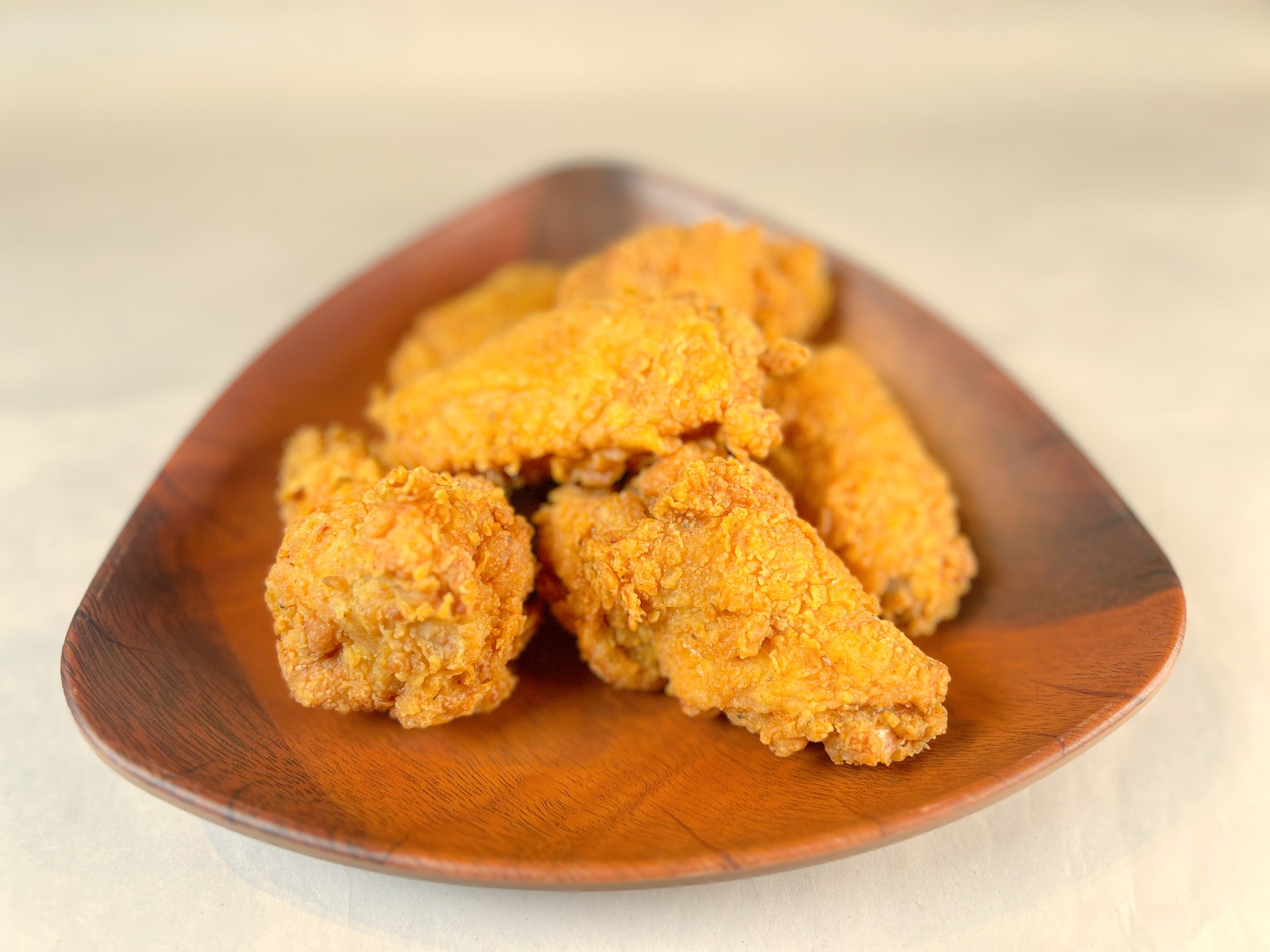 Close-up of several pieces of golden-brown fried chicken on a wooden plate.