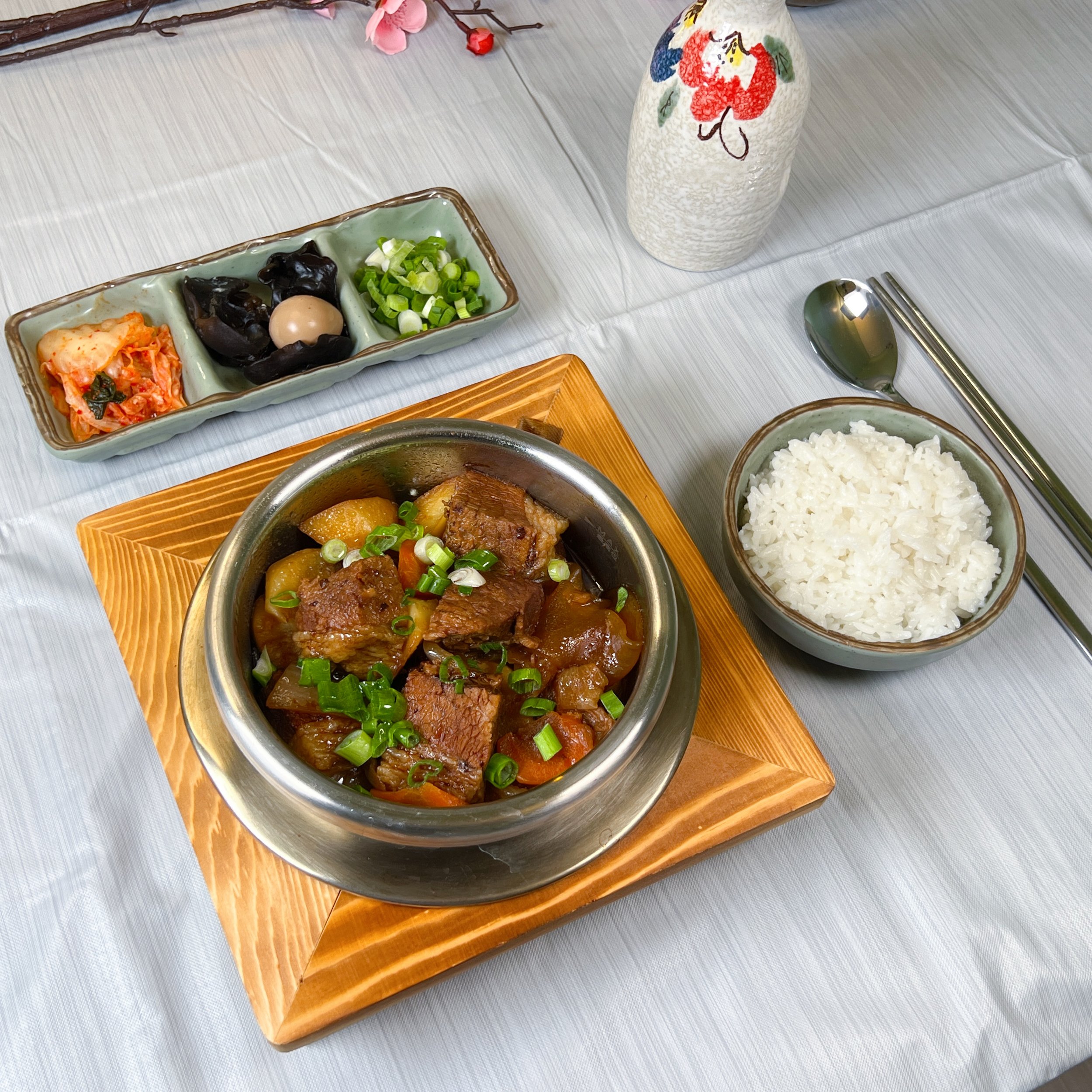 Traditional Korean side dishes and cooked ingredients on a dining table, with a ceramic vase and chopsticks.