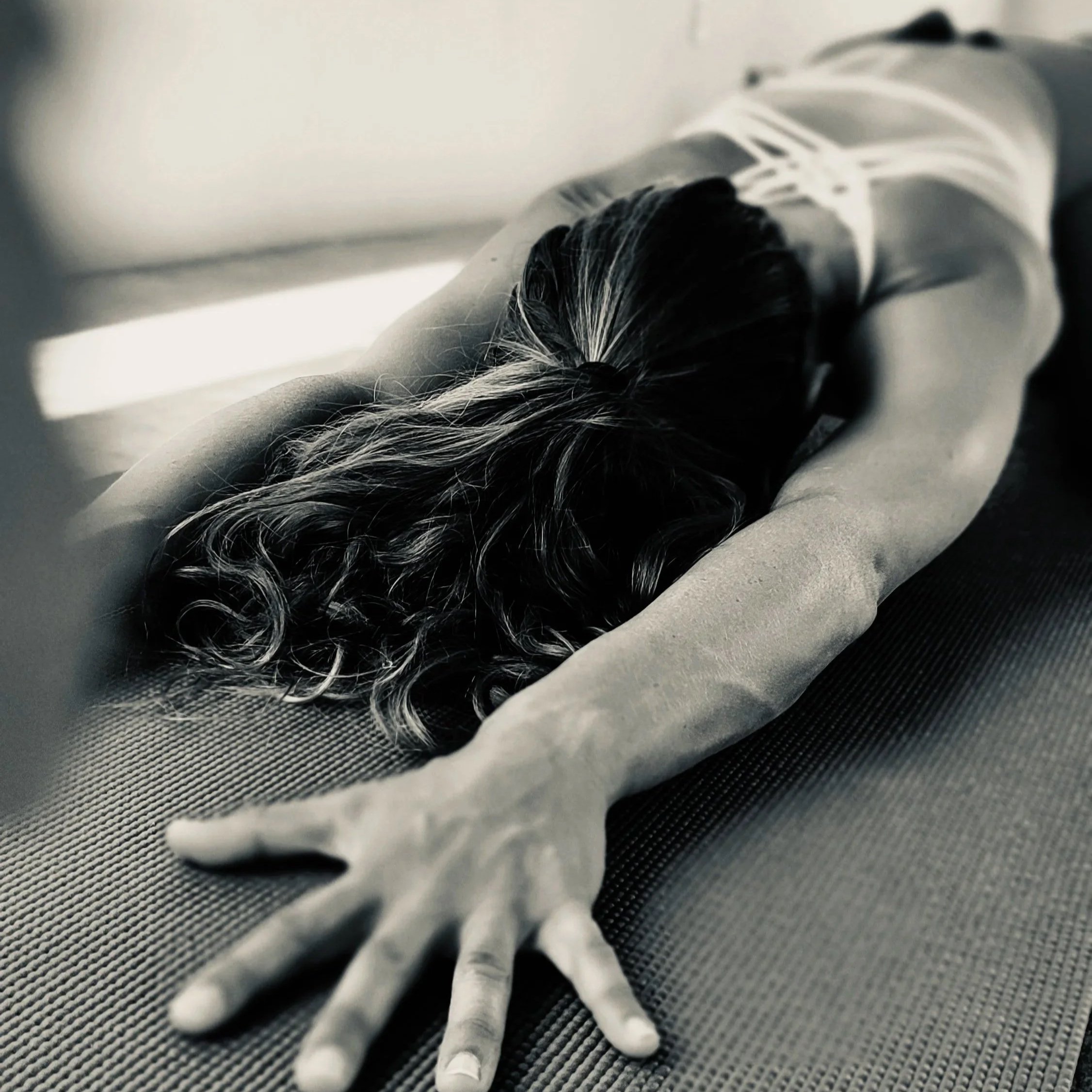 Close-up of a yoga practitioner in extended child's pose with a hands extended and palms spread on a black and gray textured surface.