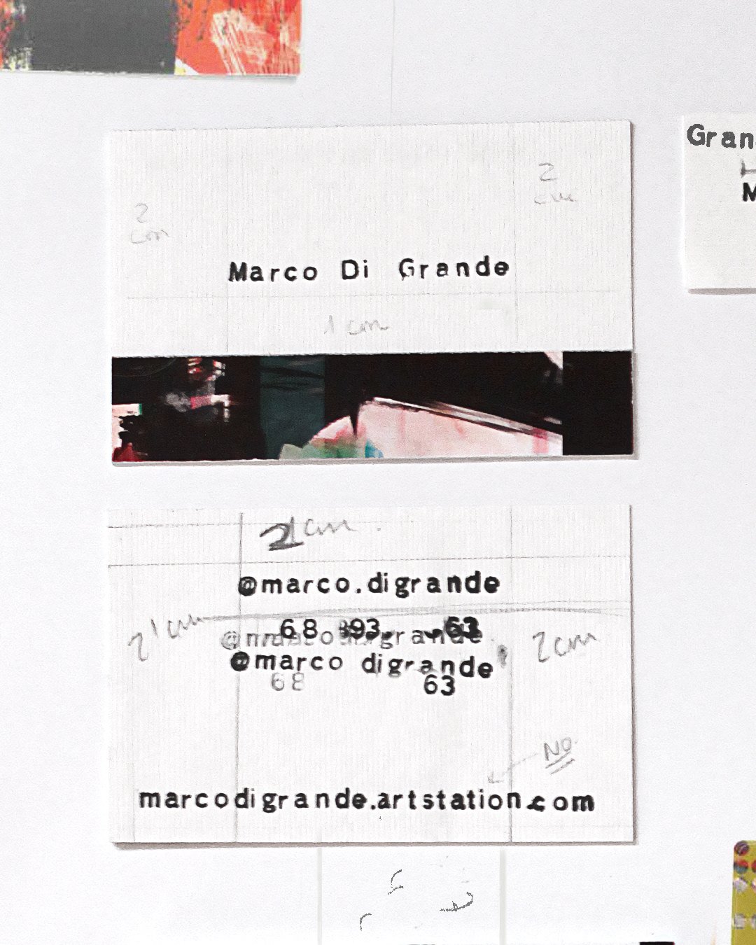 Close-up of a white paper with handwritten and printed text, including the name 'Marco Di Grande,' social media handles @marco.digrande, and a website marcodigrande.artstation.com, along with some small handwritten notes and measurements.