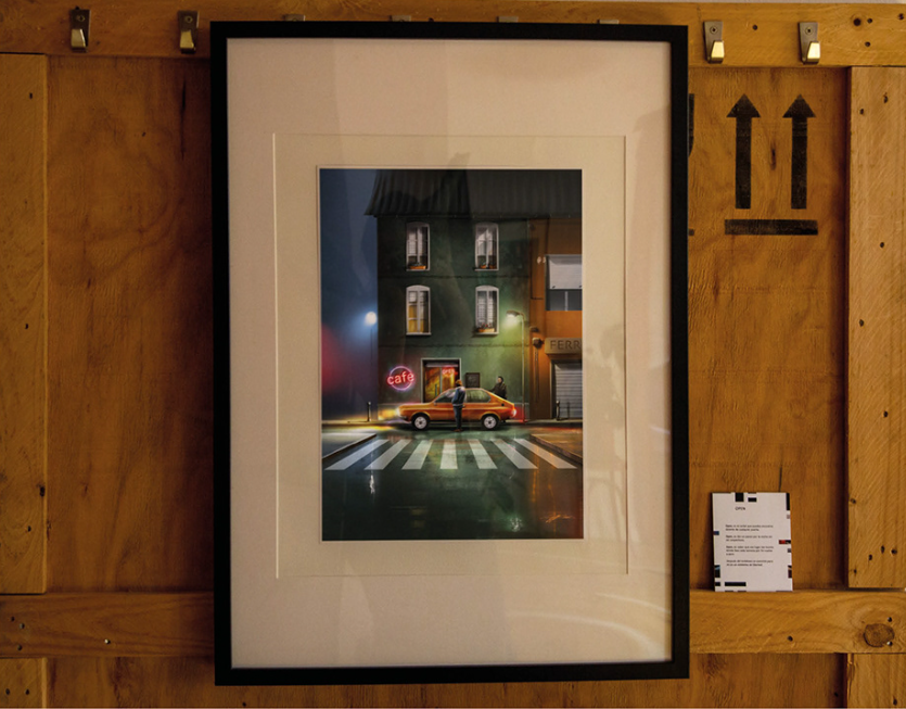 A framed digital artwork hangs on a wooden wall, depicting a nighttime city scene with a classic car at a crosswalk in front of a building with illuminated windows and a neon cafe sign.