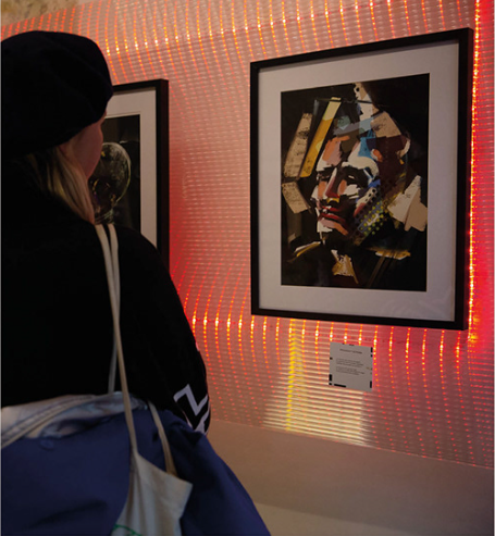 Person viewing abstract portrait artwork in a gallery with red LED lighting wall.