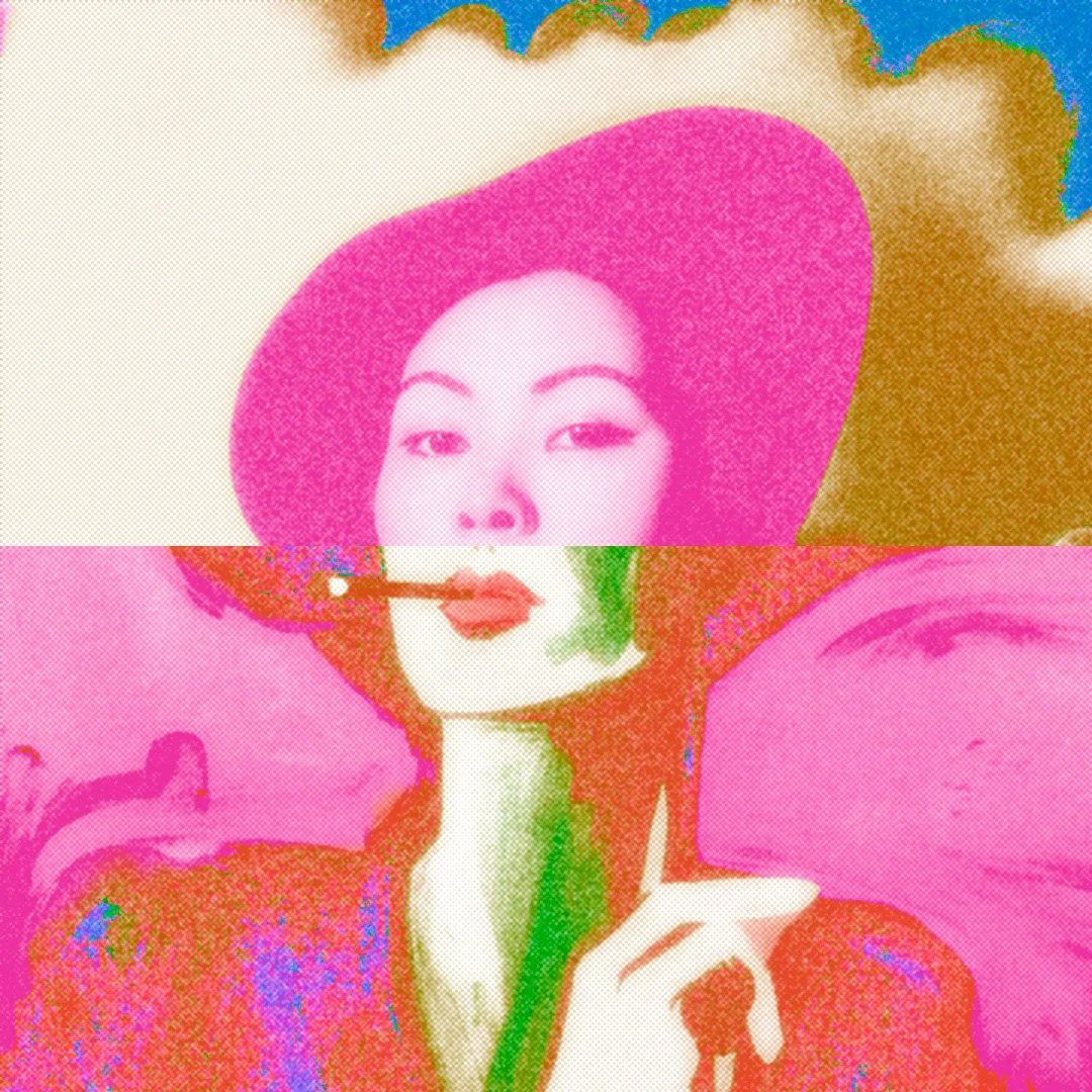 A woman wearing a large pink hat with a wide brim, holding a pink flower close to her lips, and dressed in colorful attire with pink and red hues.