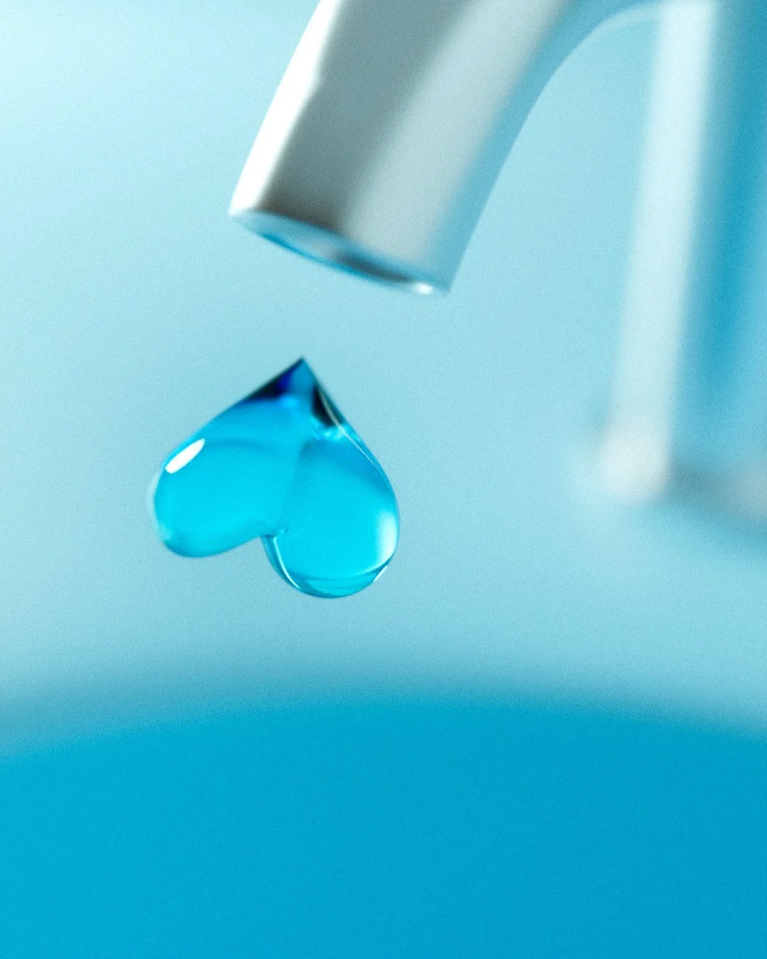 Close-up of a blue gel drop hanging from a metallic faucet, with a light blue background.