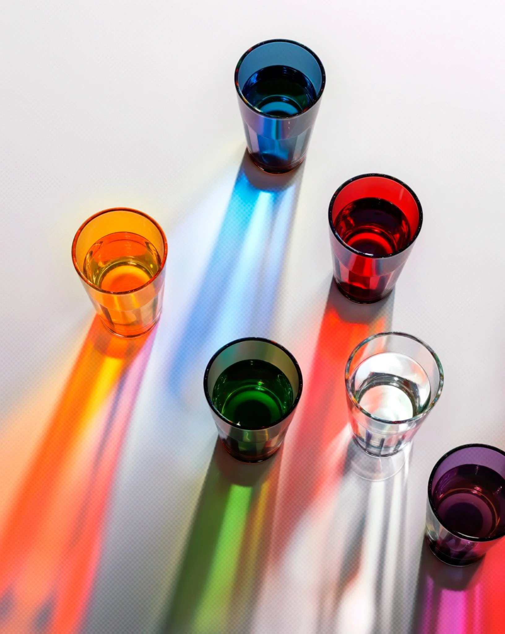 CGI render of coloured glasses casting long rainbow shadows on a white surface