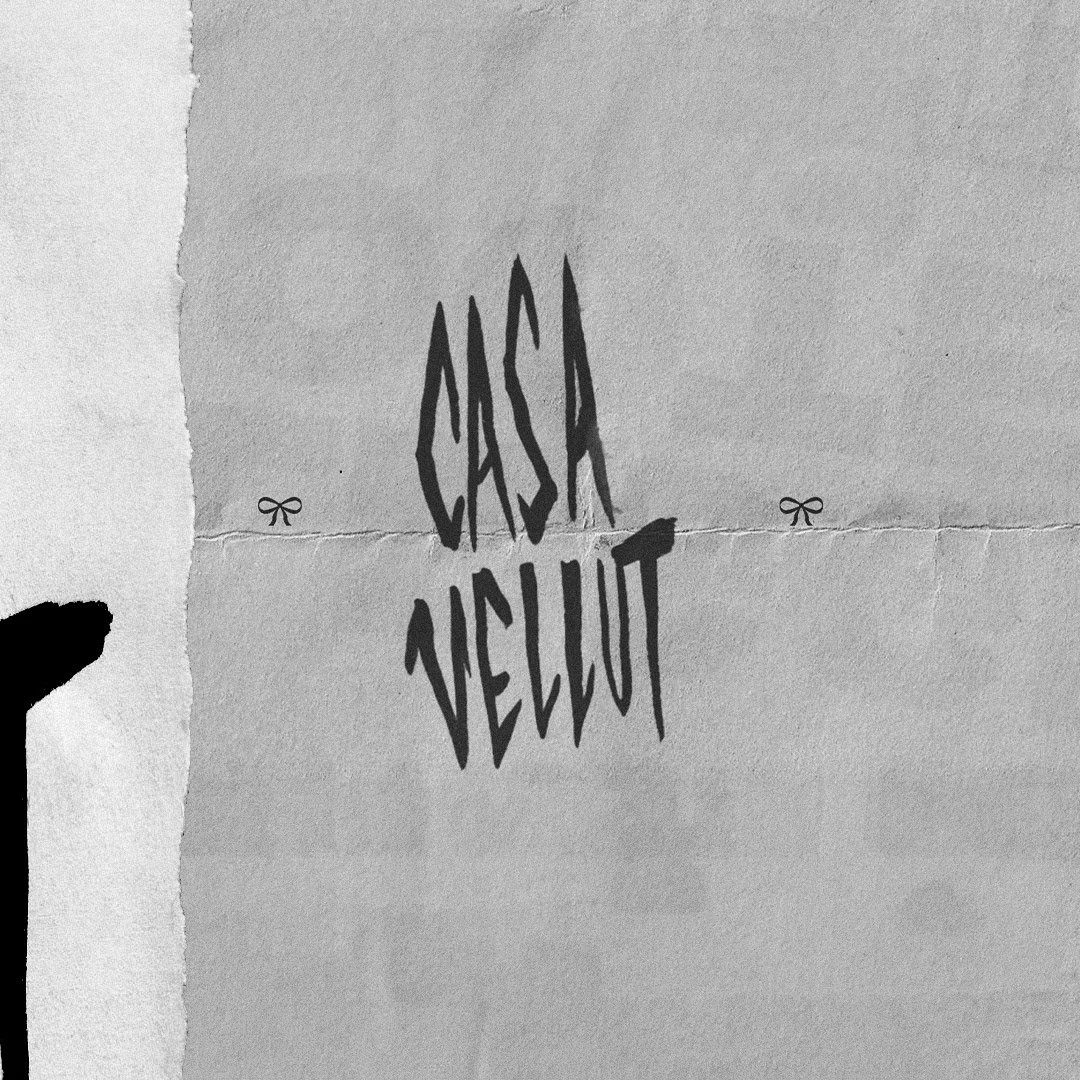 Paper with the words 'CASKA VELUT' written in black, shadowed letters, and small bow illustrations on either side.