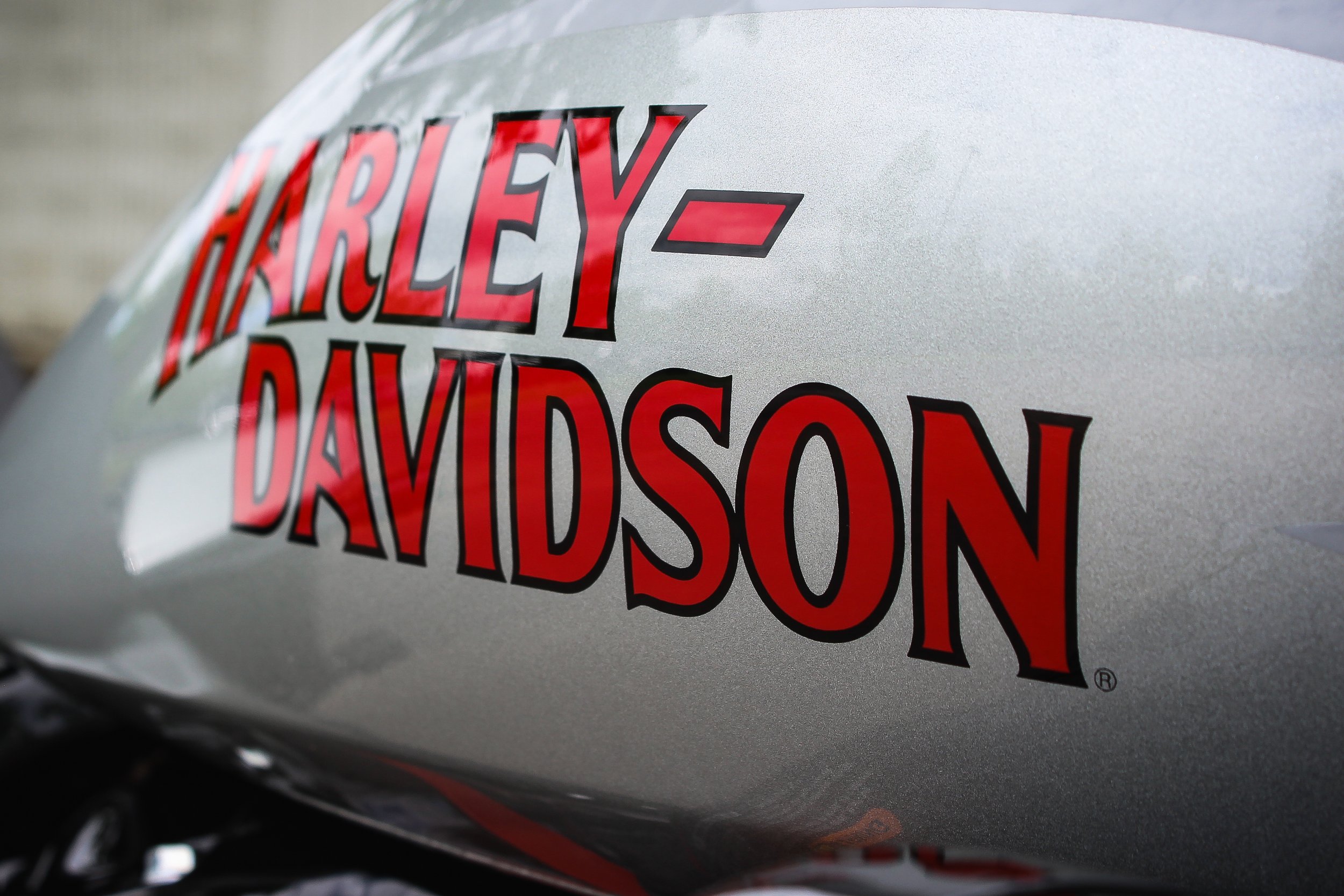 Close-up of a silver motorcycle tank with a red and black Harley-Davidson logo decal.