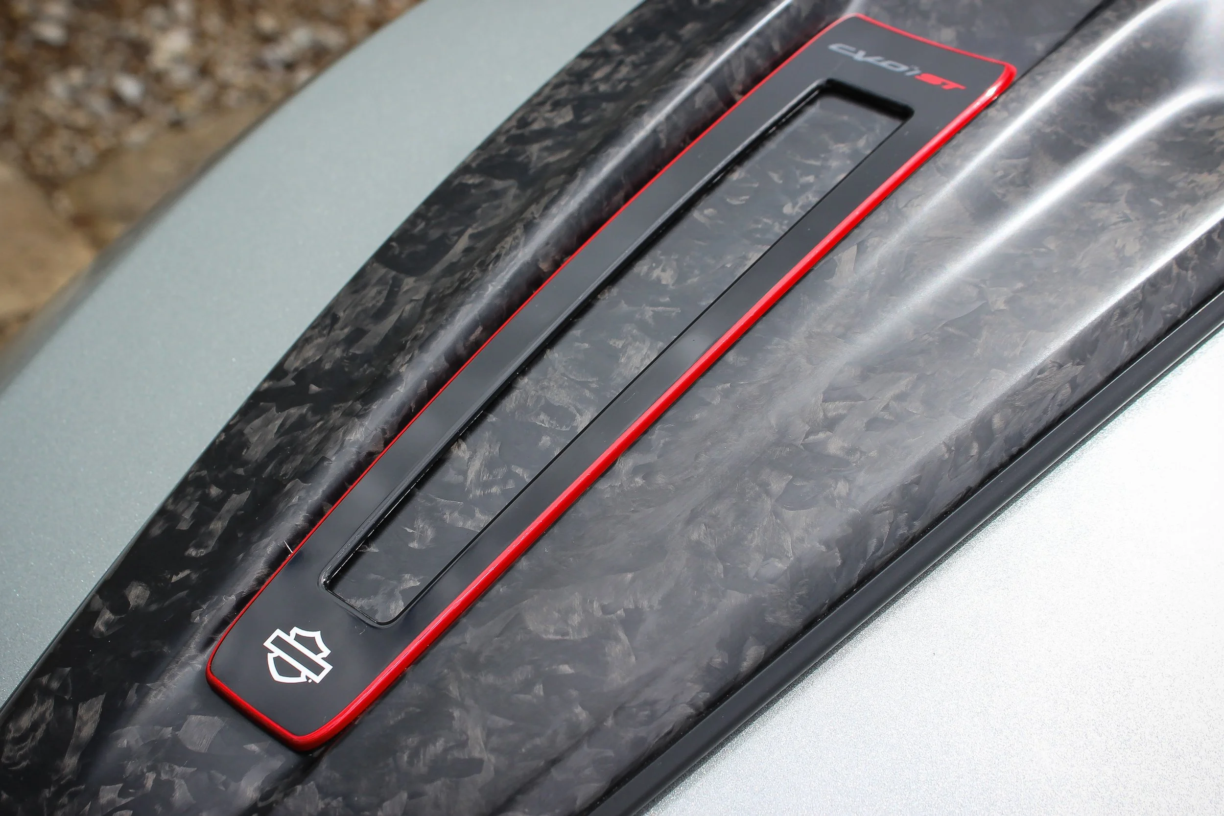 Close-up of a black and red Harley-Davidson motorcycle component with a textured black surface and a smooth black panel with a red border, marked with a white Harley-Davidson logo.