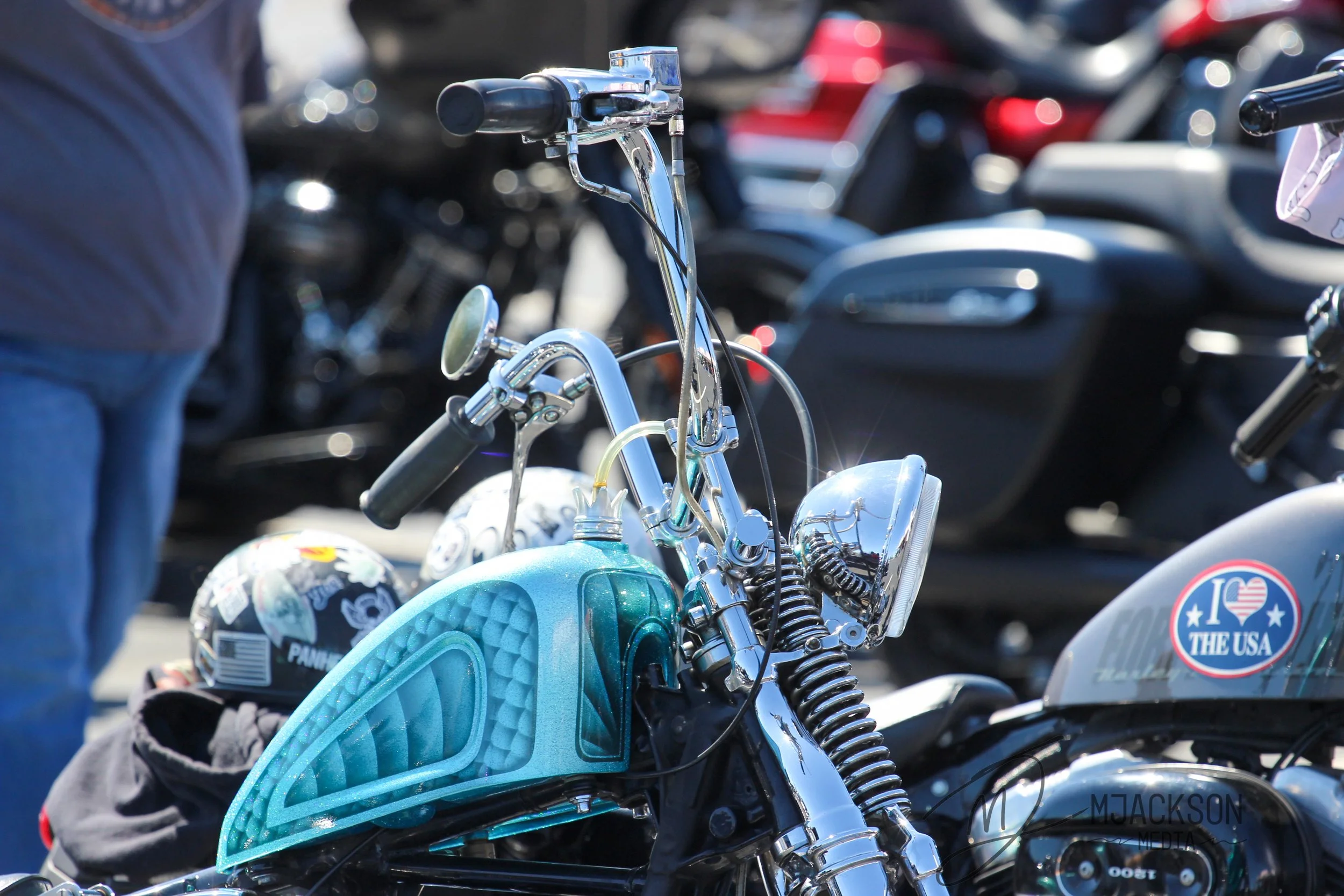 Close-up of a shiny motorcycle handlebar and fuel tank with a blue disc-style helmet and a motorcycle helmet with stickers.