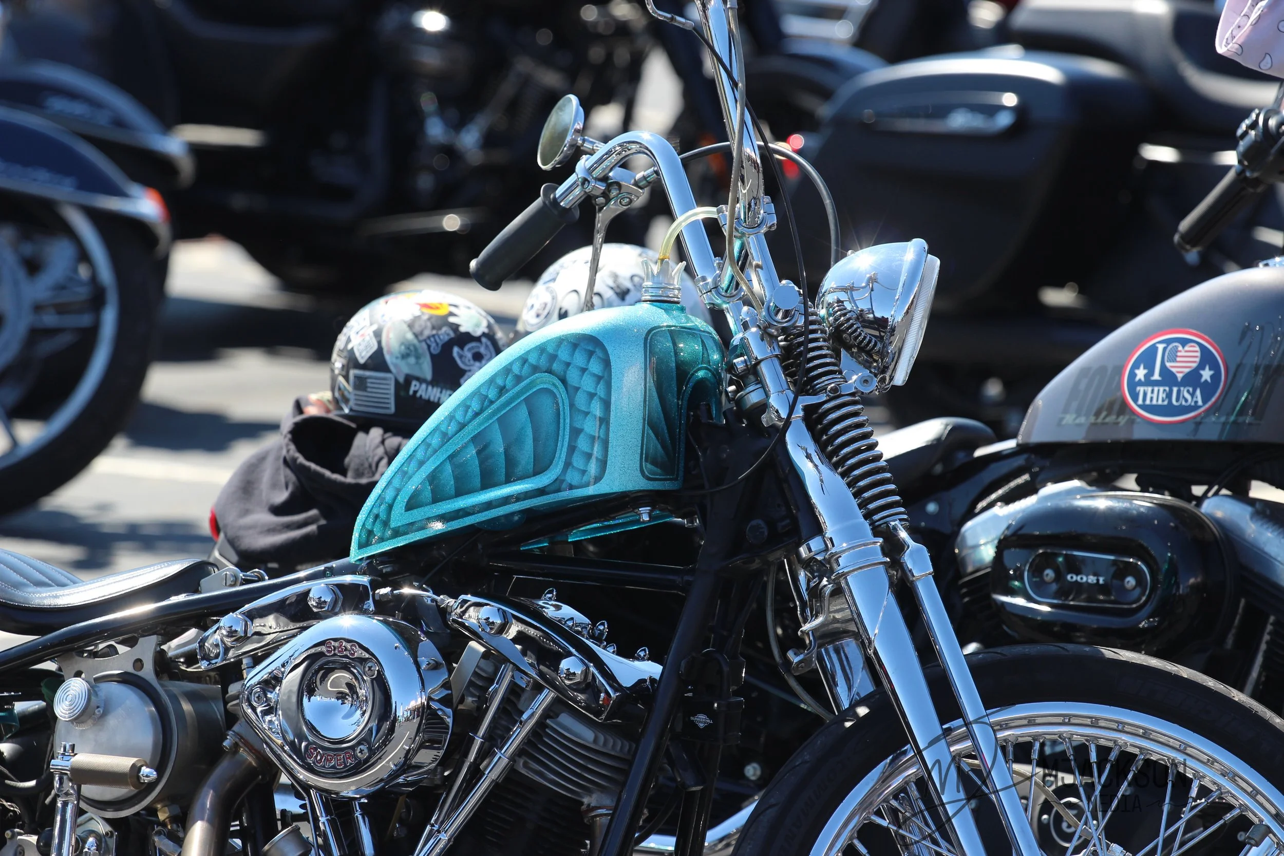 A close-up of multiple motorcycles parked outdoors, featuring shiny chrome parts, helmets, and United States-themed stickers.
