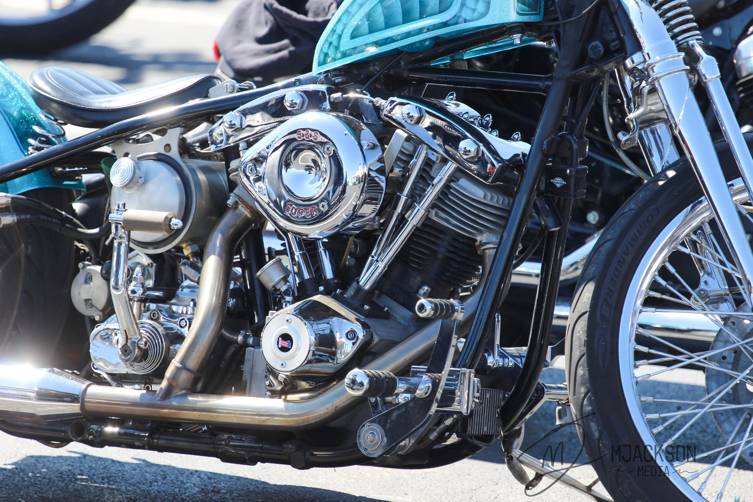 Close-up of a shiny chrome motorcycle engine and parts, with a black leather seat and front wheel visible.