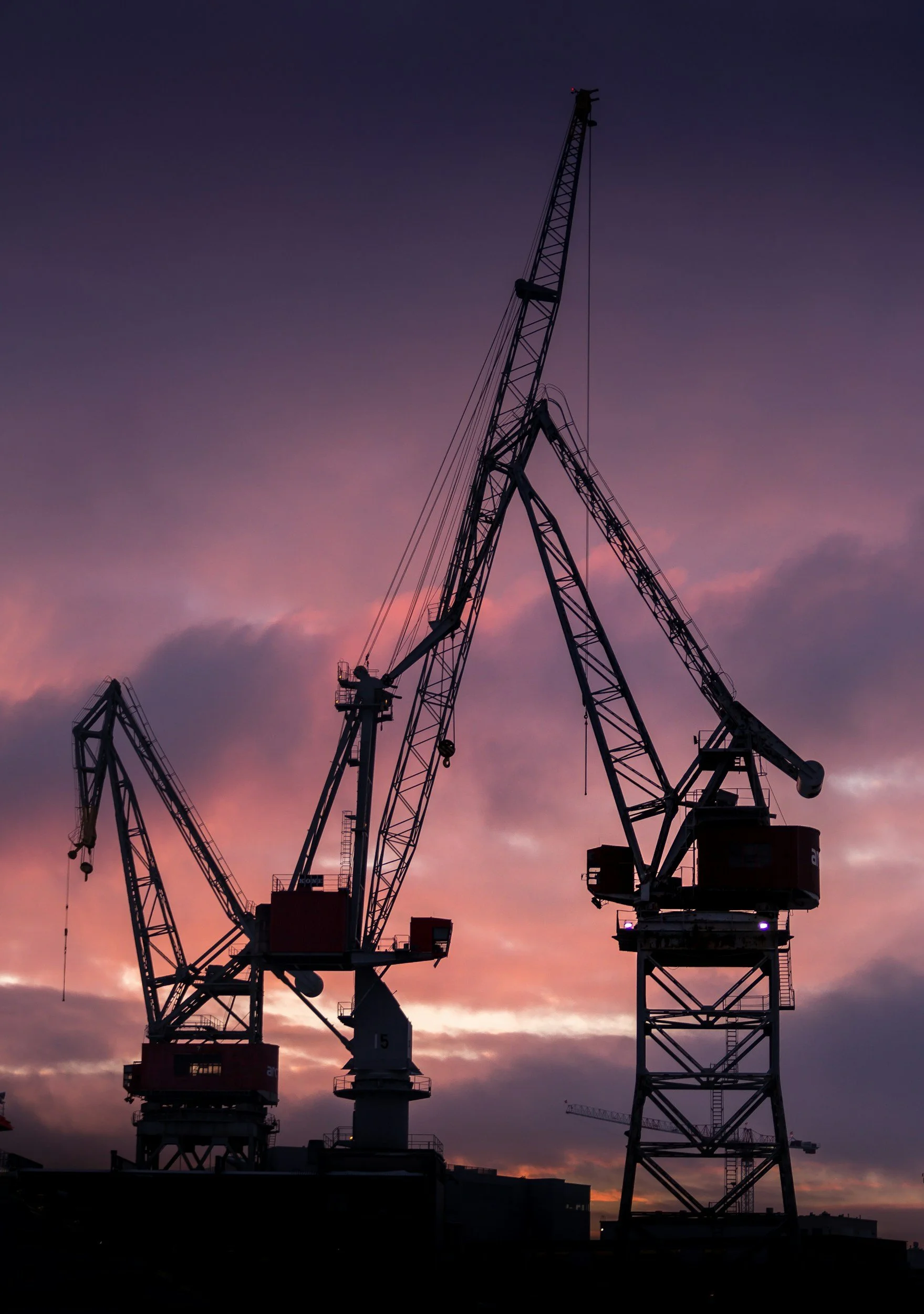 Silhouettes of shipyard cranes against a colorful sunset sky.