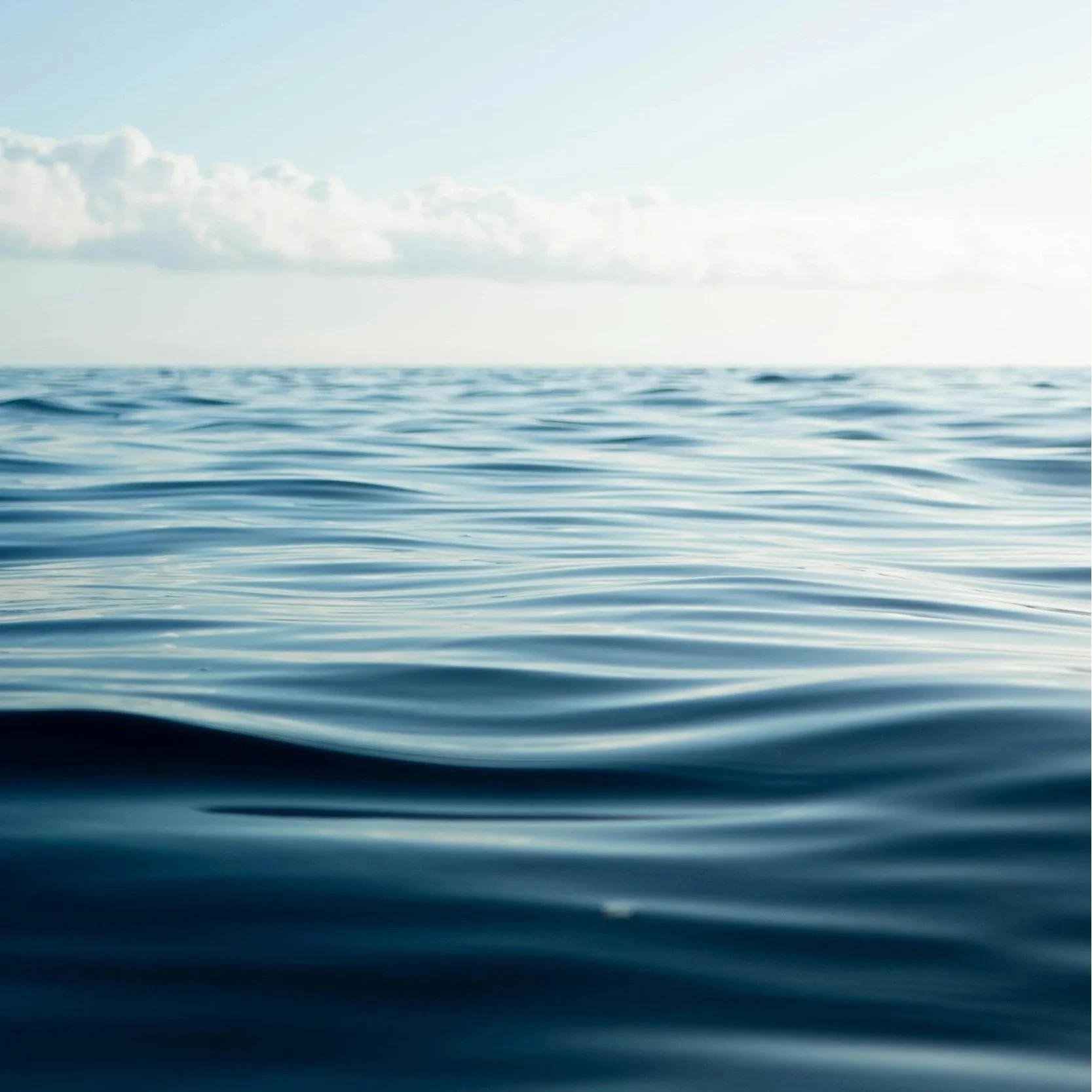 Calm ocean water with gentle waves and a partly cloudy sky.