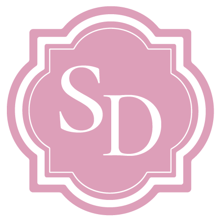 Pink decorative emblem with white outline and the initials 'SD' in white