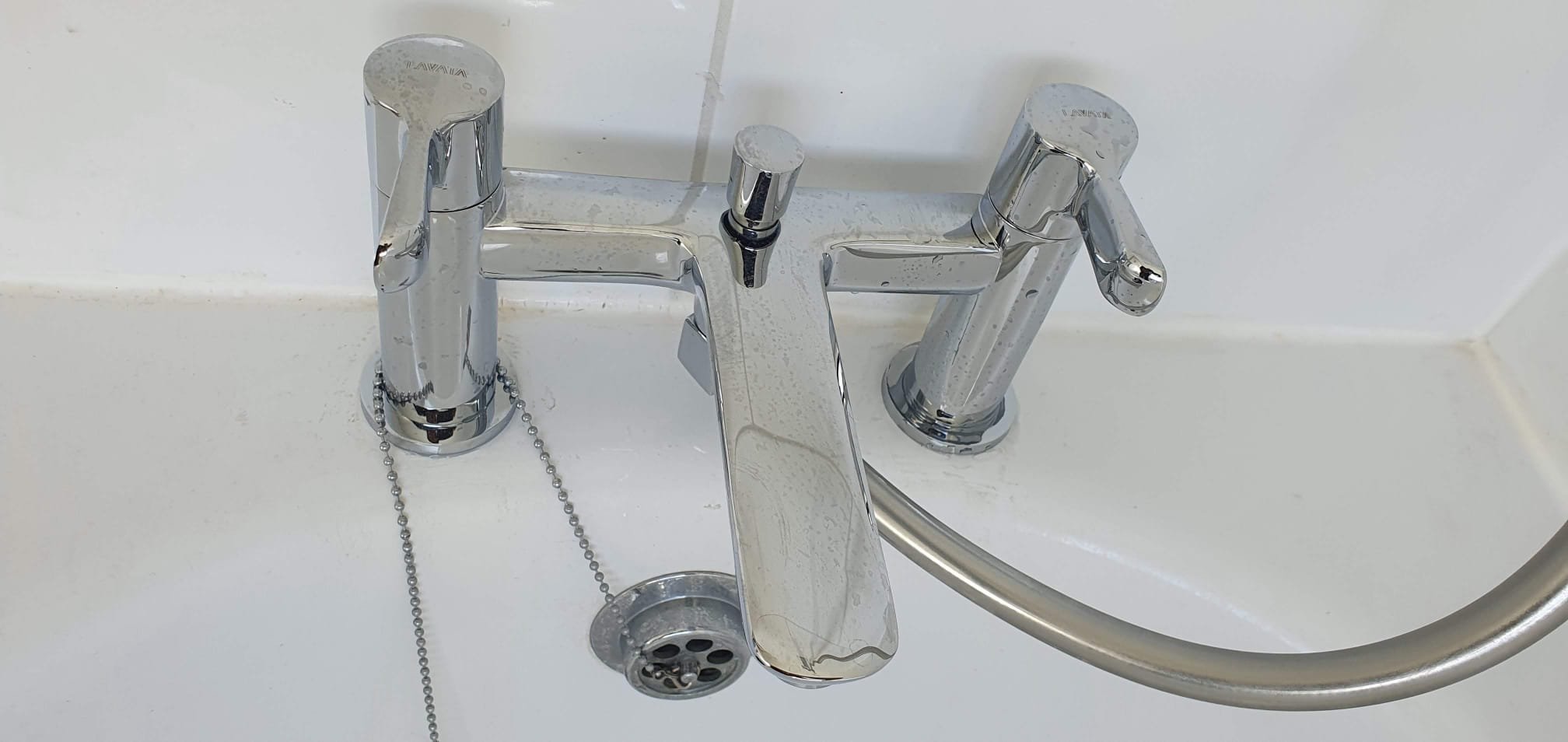Chrome bathtub faucet with separate hot and cold handles, handheld shower hose, and chain-operated drain plug.