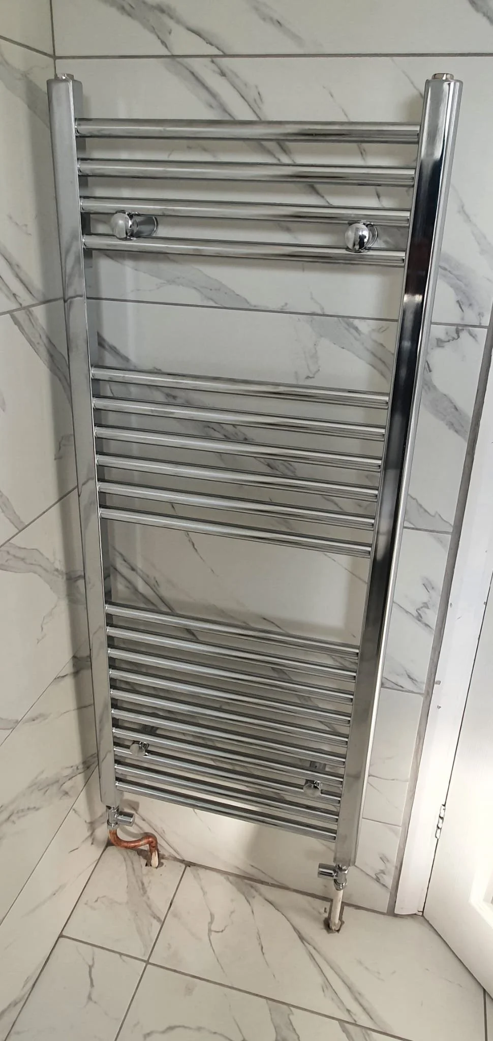 Chrome heated towel radiator mounted on a marble-look tiled bathroom wall