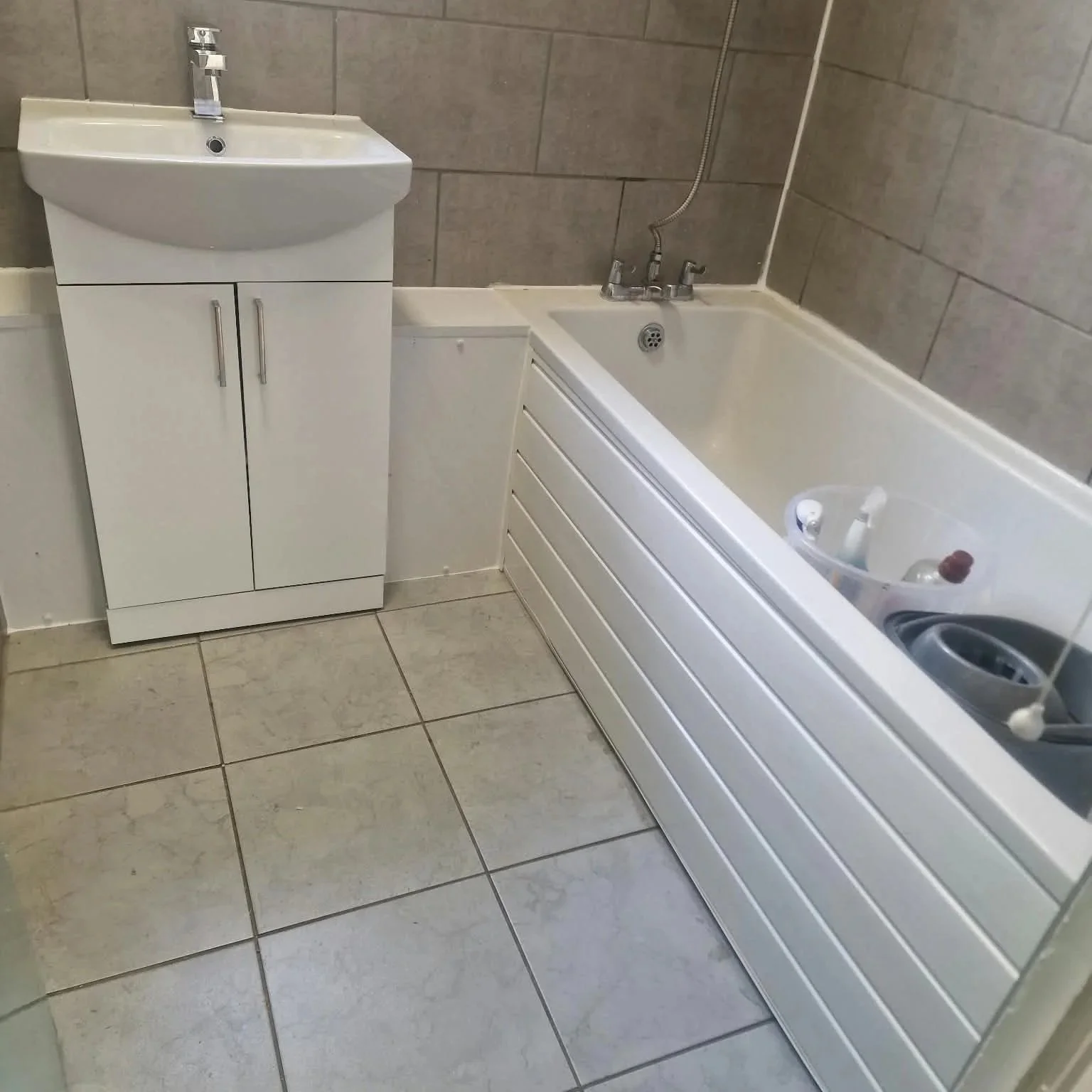 White bathroom sink vanity beside a bathtub with tiled walls and floor