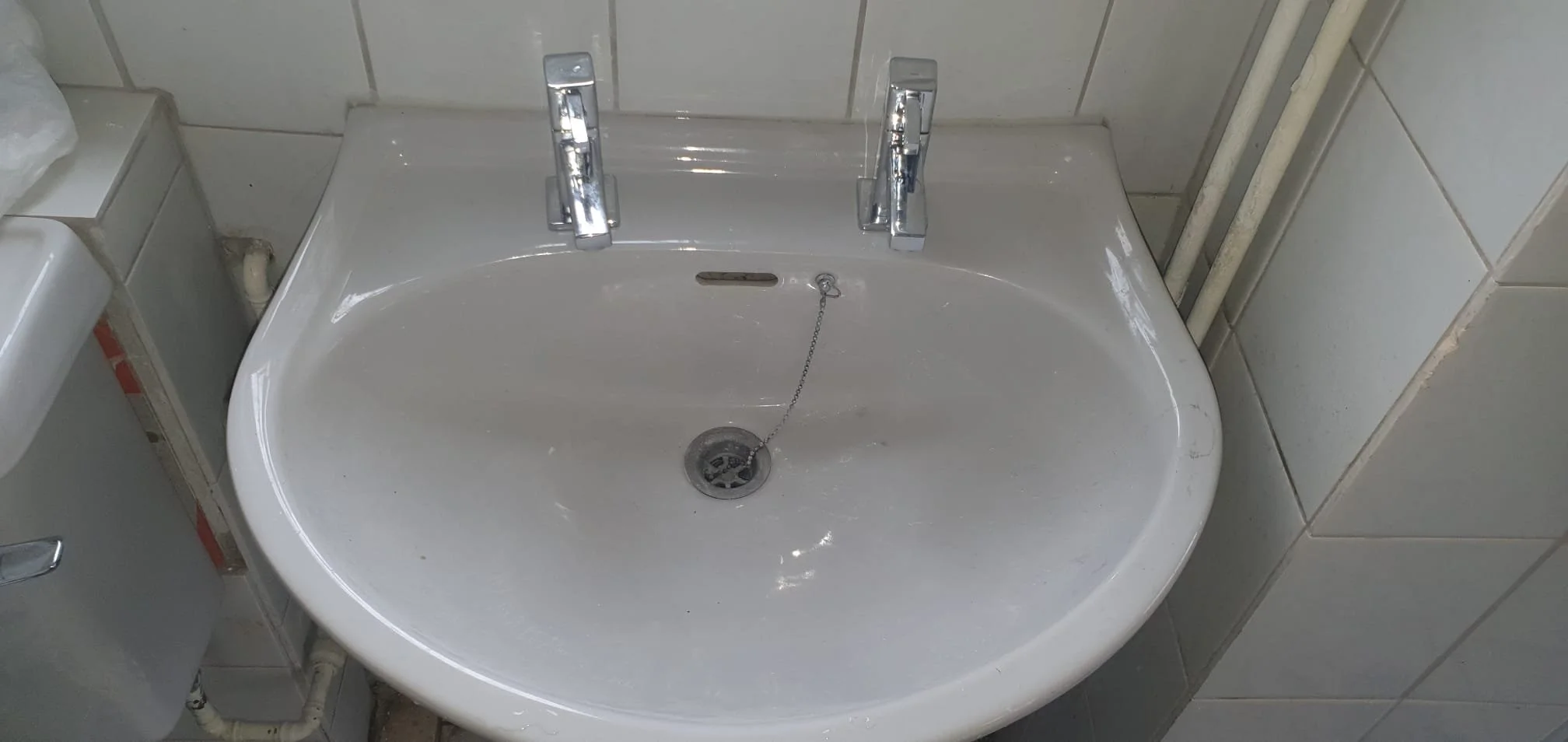 White ceramic bathroom sink with twin chrome faucets and chain-linked drain plug