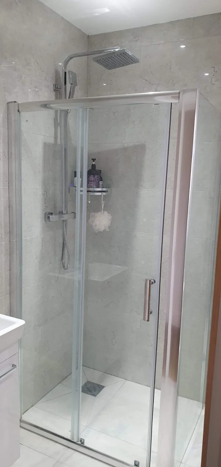 Modern glass-enclosed bathroom shower with rainfall showerhead, handheld spray, soap dispenser, and tiled walls