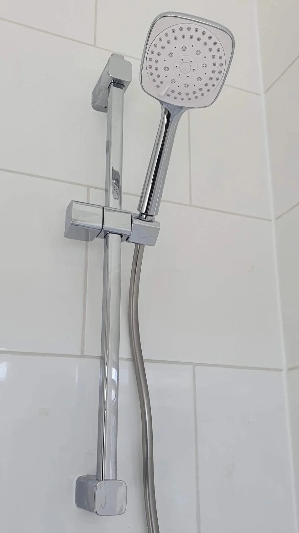 Chrome handheld showerhead mounted on a tiled bathroom wall with adjustable slide bar and flexible hose