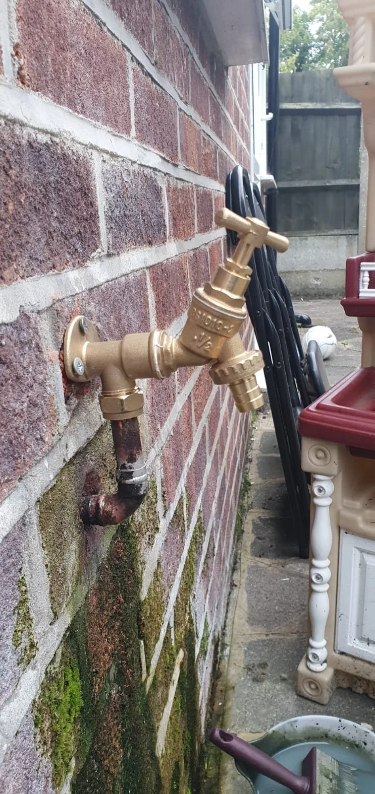 Outdoor brass garden faucet mounted on a moss-covered brick wall