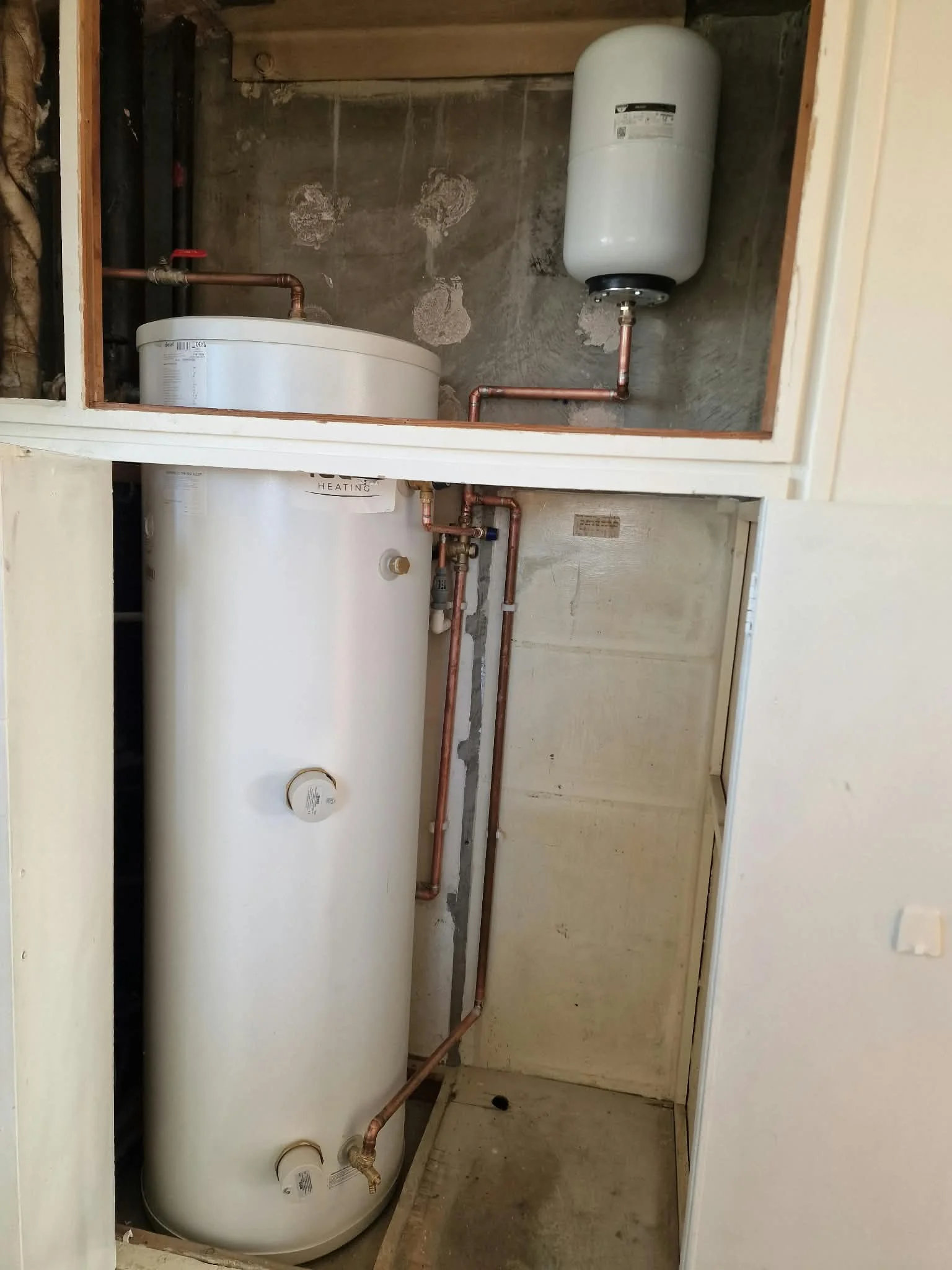 Large white hot water storage tank with copper plumbing and expansion vessel in a utility closet