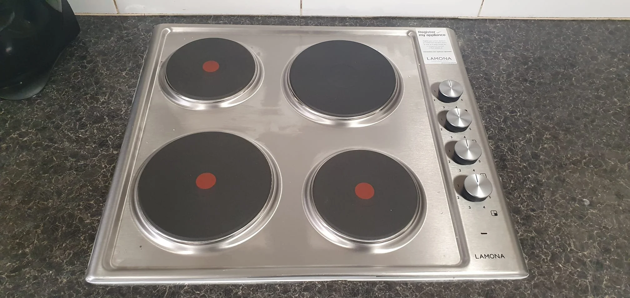 Stainless steel Lamona four-burner electric cooktop with four control knobs on a dark kitchen countertop