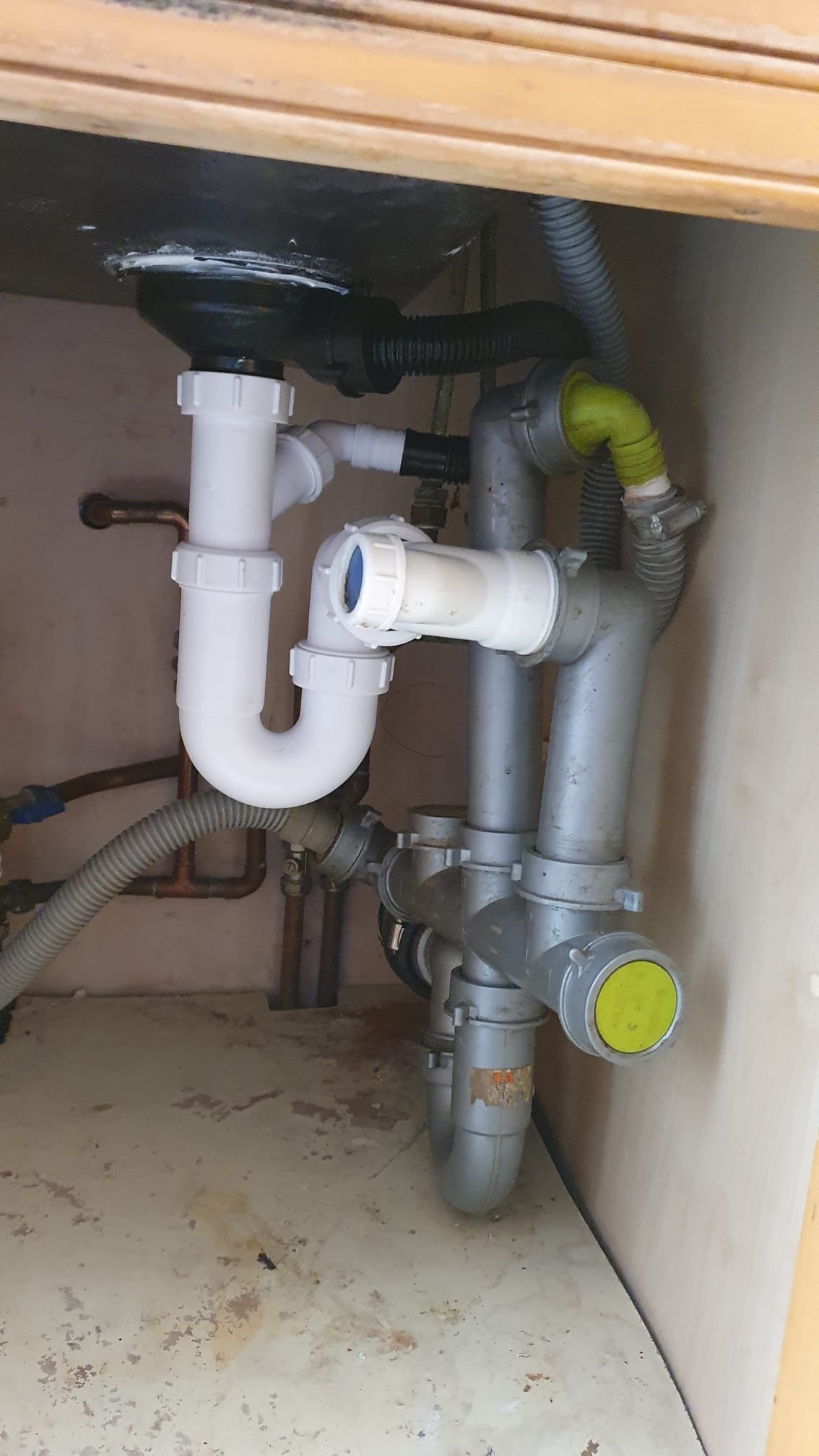 Under-sink plumbing with a white P-trap, drain pipes, flexible hoses, and dishwasher connections.