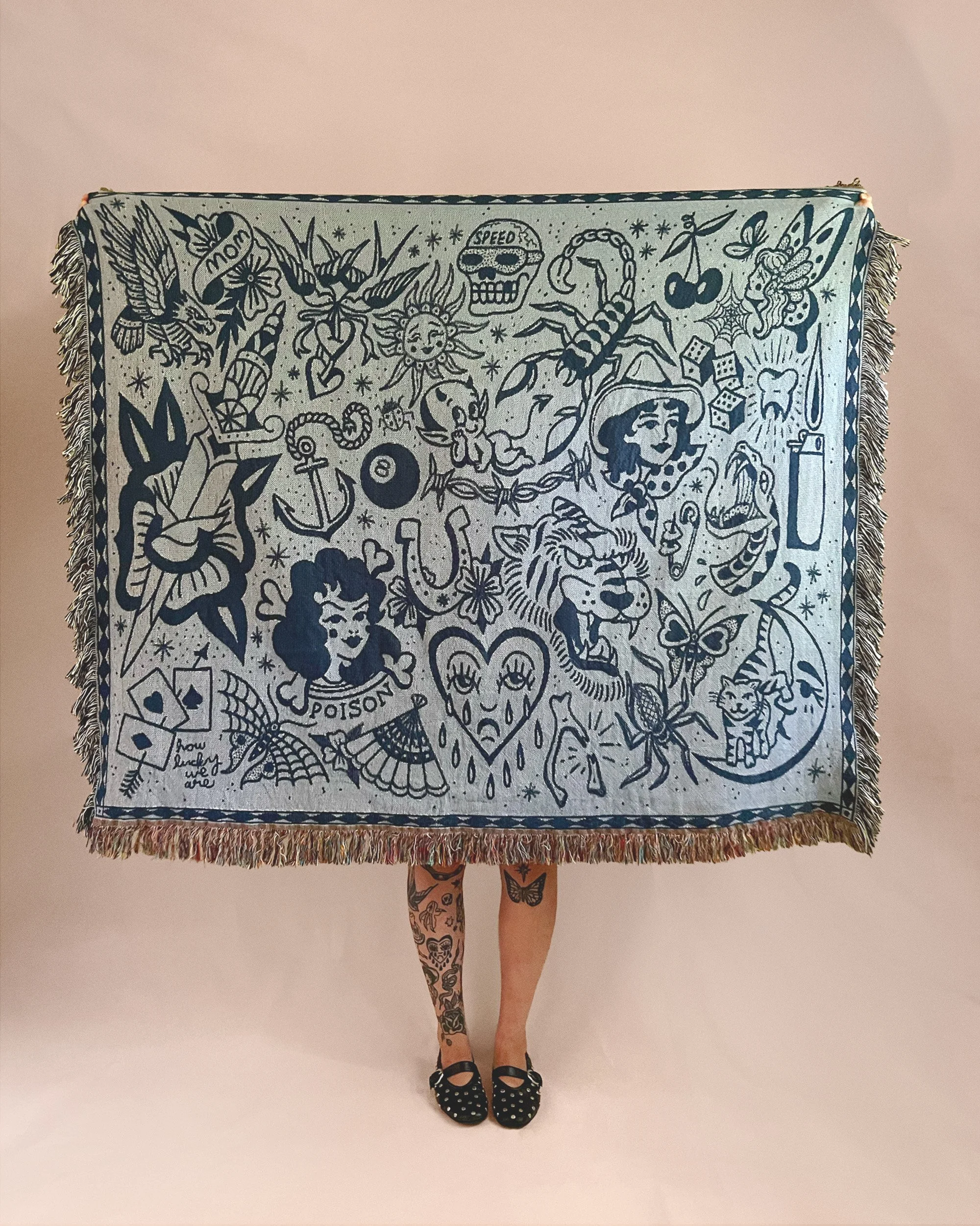 Dress with a tattooed woman standing against a white background. The dress has a black and white tattoo-style illustration, featuring various figures and symbols, including a dragon, a skull, a sun with a face, a woman with butterfly wings, animals, and words like "mom," "poison," "speed," and "love." The woman wears black open-toe shoes with white polka dots and has tattooed legs.