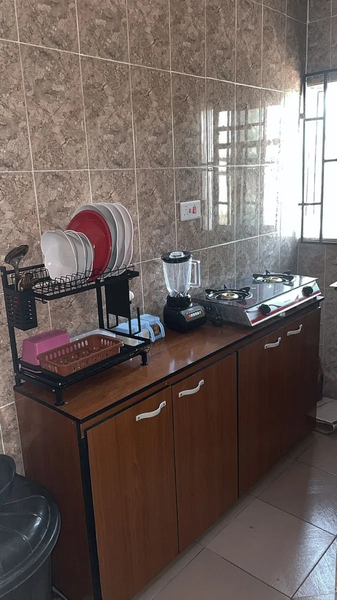Kitchen countertop with a dish rack, blender, stove, and cabinets, near a window with metal bars.